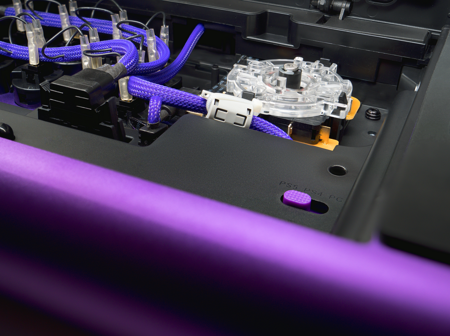 Primer plano del interior de un mando de juegos morado. Cables y un botón visibles.