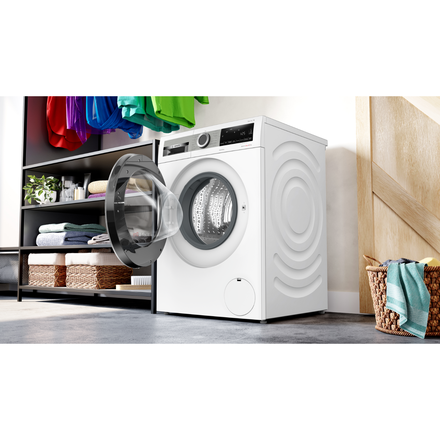 Witte wasmachine met open deur, kleding in de mand. Kleurrijke kleding hangt op een rek op de achtergrond.