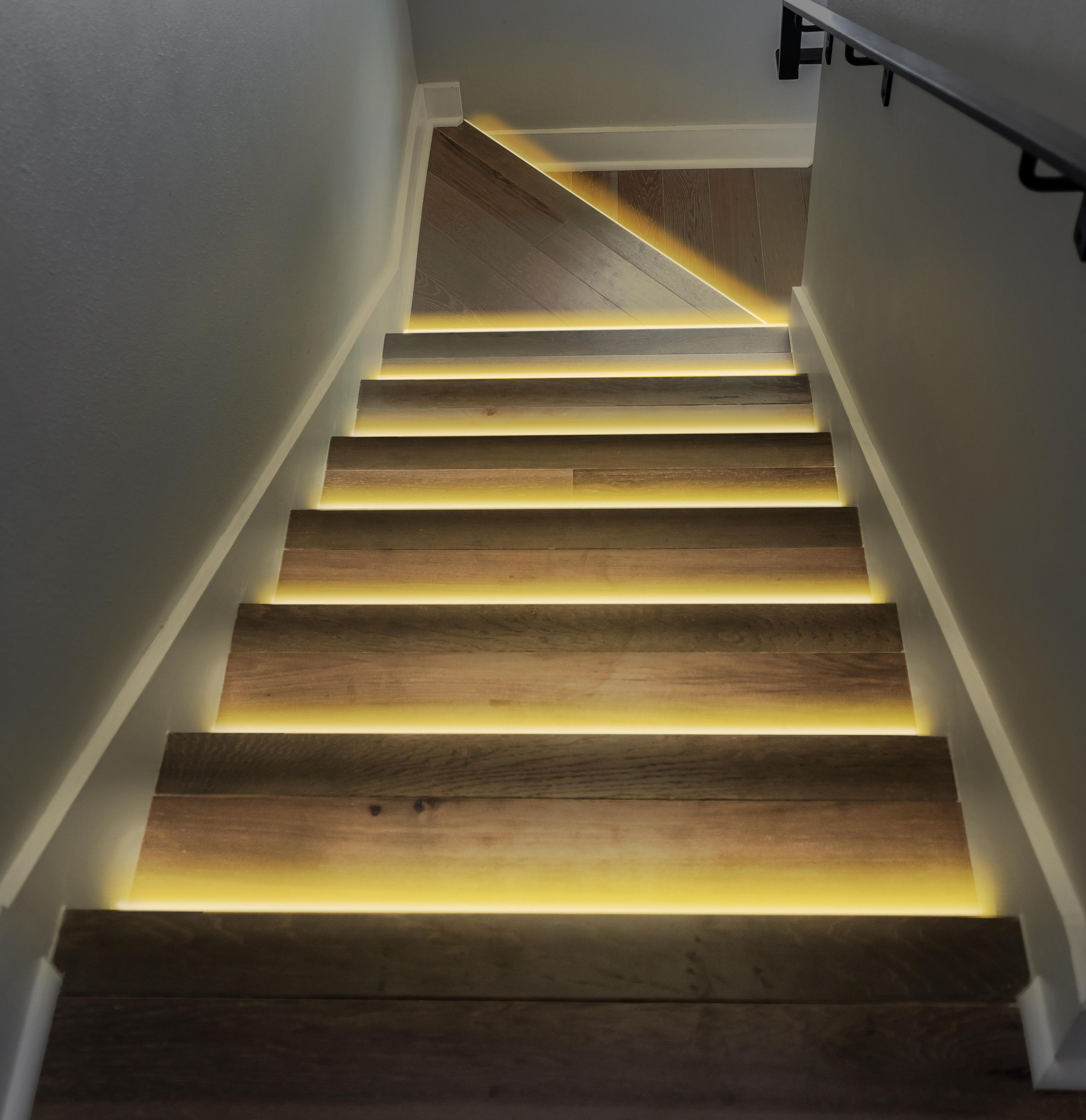 Treppe mit Holzstufen und gelben Lichtern. Wand und Decke sind weiß.