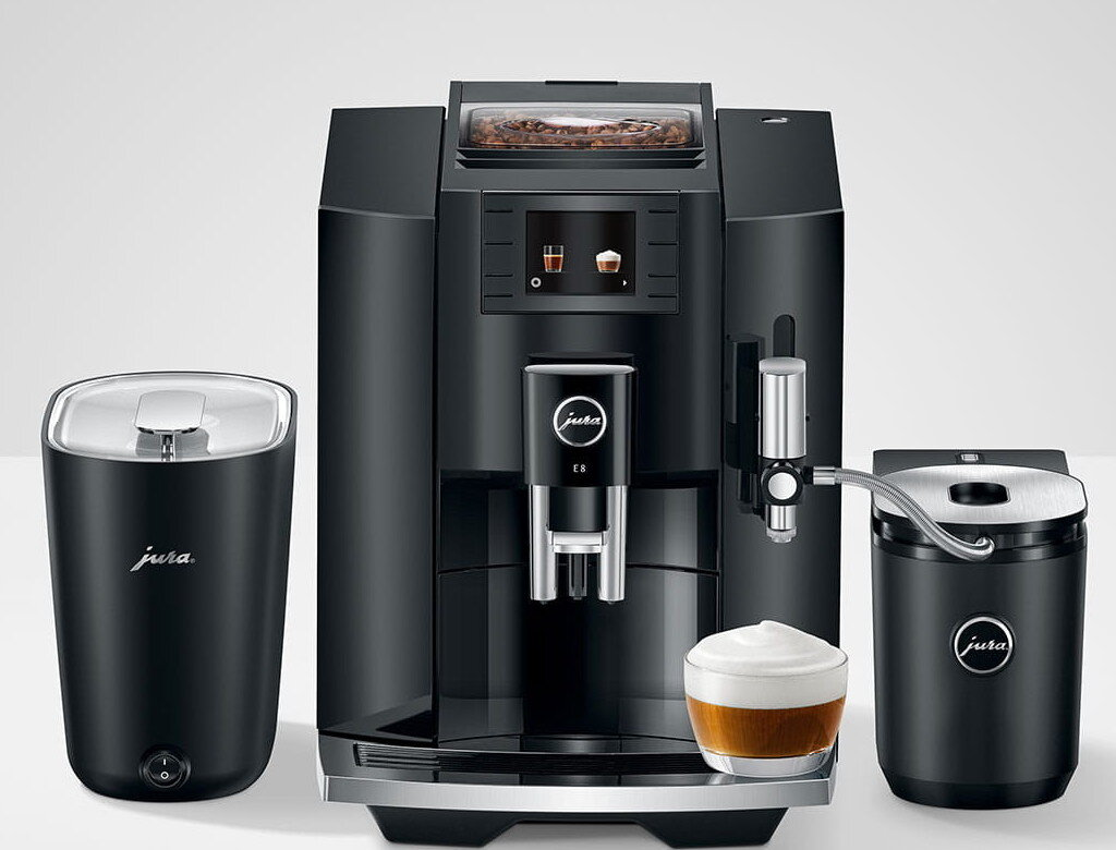Czarny ekspres do kawy Jura z młynkiem i spieniaczem do mleka. Szklanka kawy z pianką stoi z przodu.