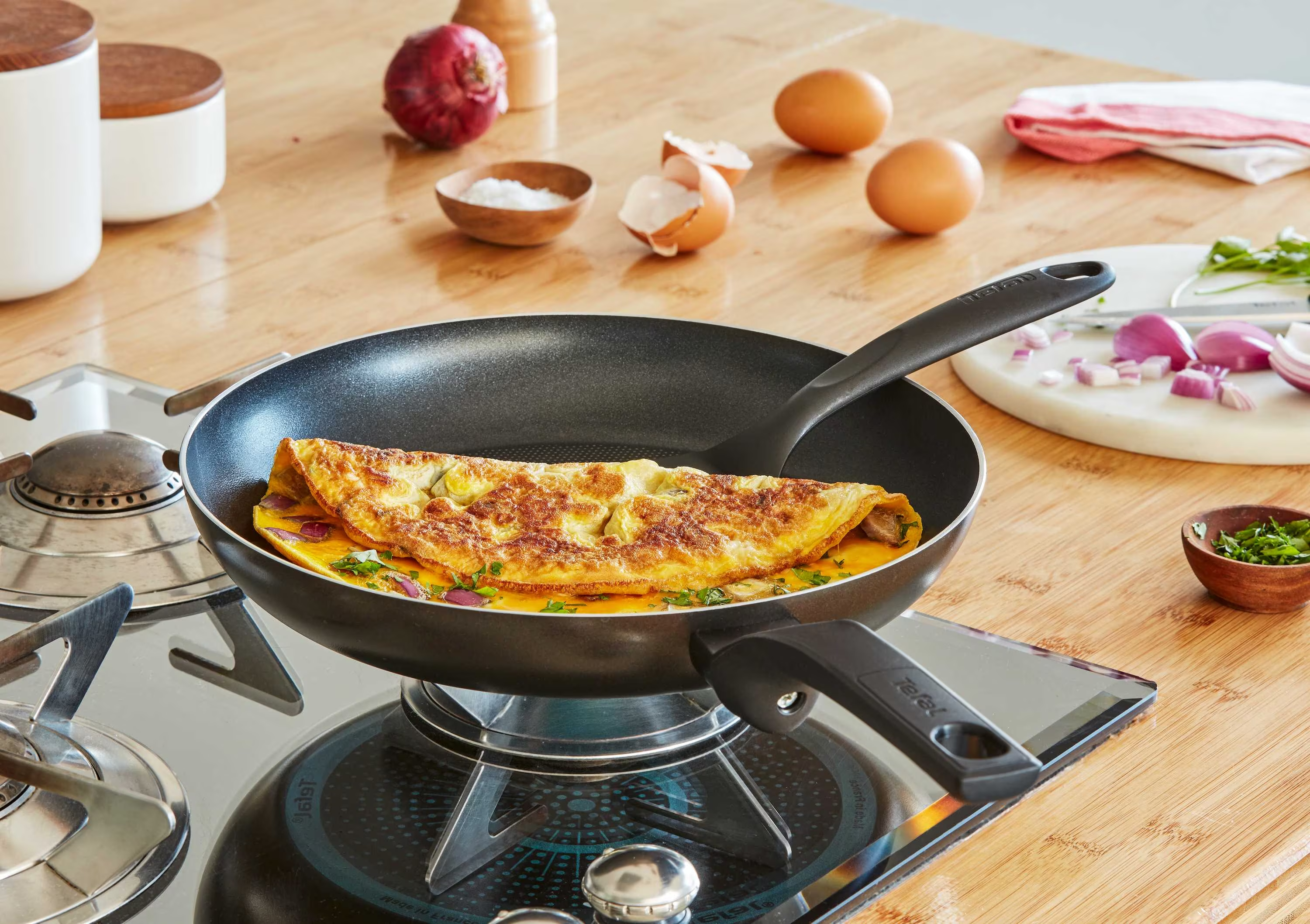 Omelette dans une poêle sur une cuisinière. Des ingrédients comme l'oignon et les herbes sont également présents.