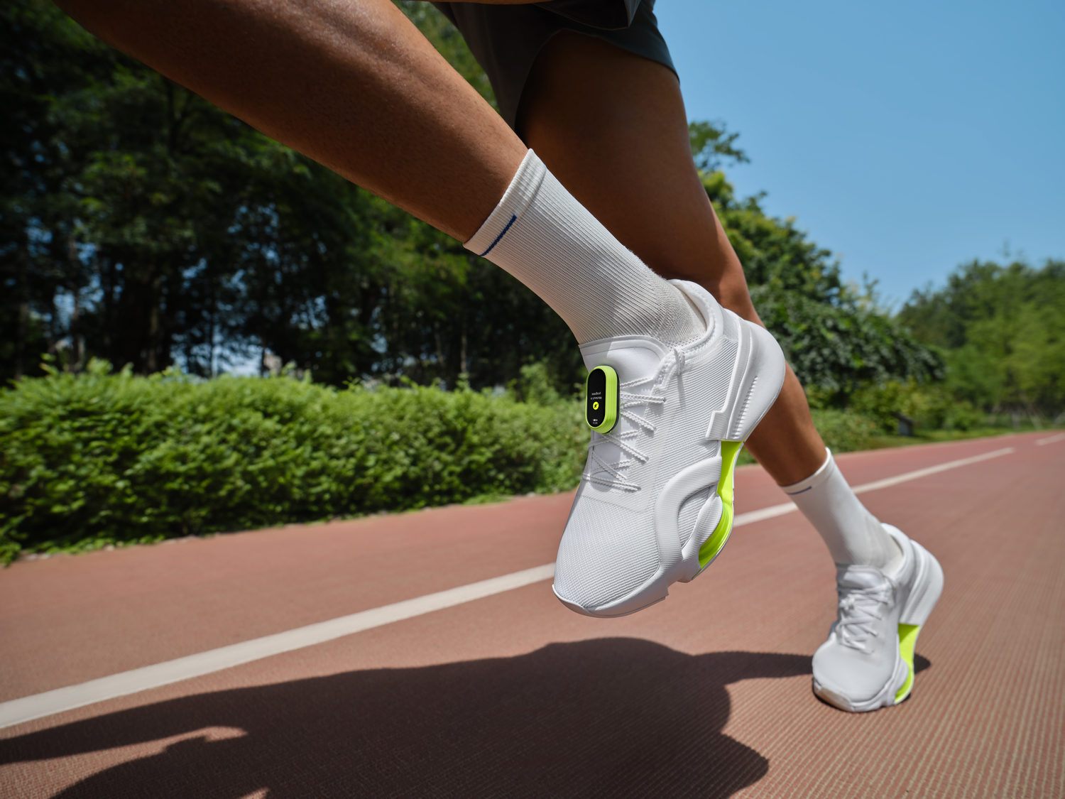 Atleta corriendo en una pista. Llevan zapatos blancos con detalles verde neón y calcetines.