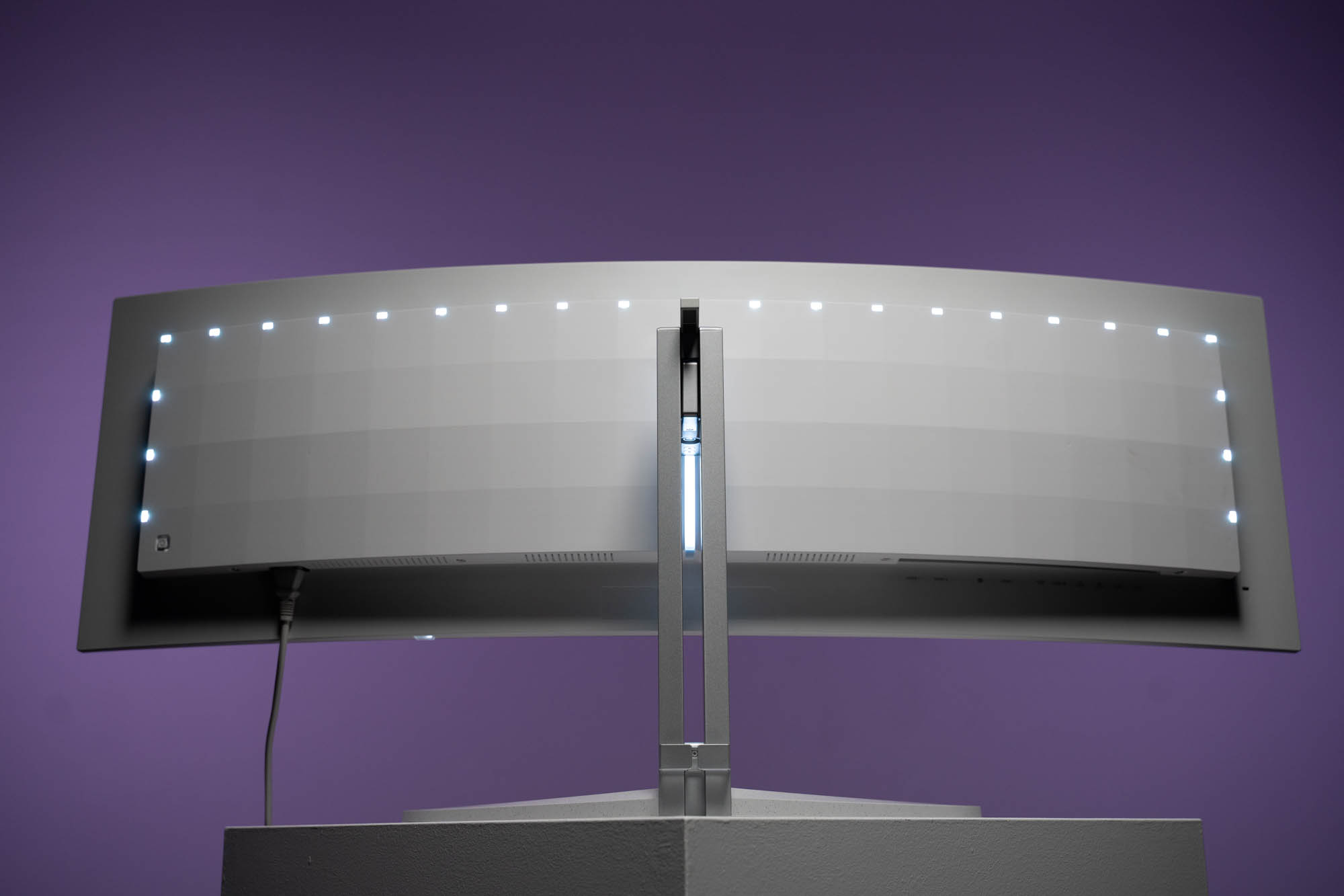 Gebogener weißer Monitor mit LED-Leuchten entlang der Oberkante. Der Monitor befindet sich vor einem lila Hintergrund.