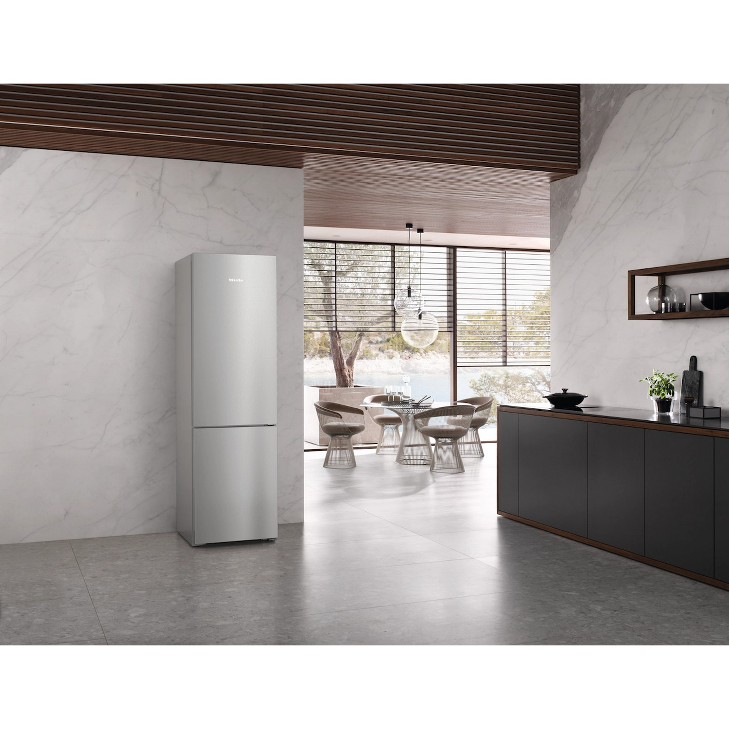 Een moderne keuken met een roestvrijstalen koelkast. Een tafel en stoelen zijn zichtbaar door een raam. Donkere kasten rechts.