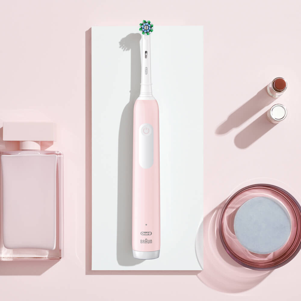 Elektryczna szczoteczka do zębów z różowymi akcentami, obok produktów do pielęgnacji skóry.
