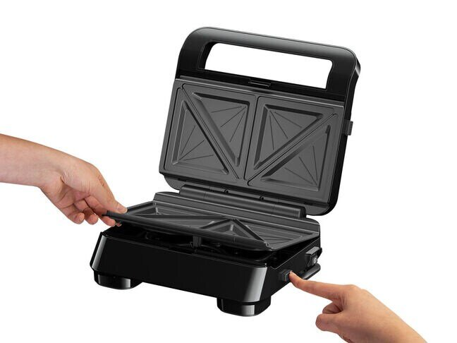 Czarny opiekacz do kanapek jest otwarty. Widać dłonie i naciska się przycisk.