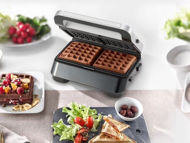 Gofrownica z upieczonymi goframi i innymi produktami spożywczymi na stole.