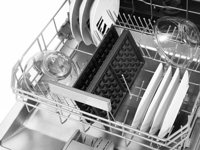 Wnętrze zmywarki z naczyniami, gofrownicą i szklankami.