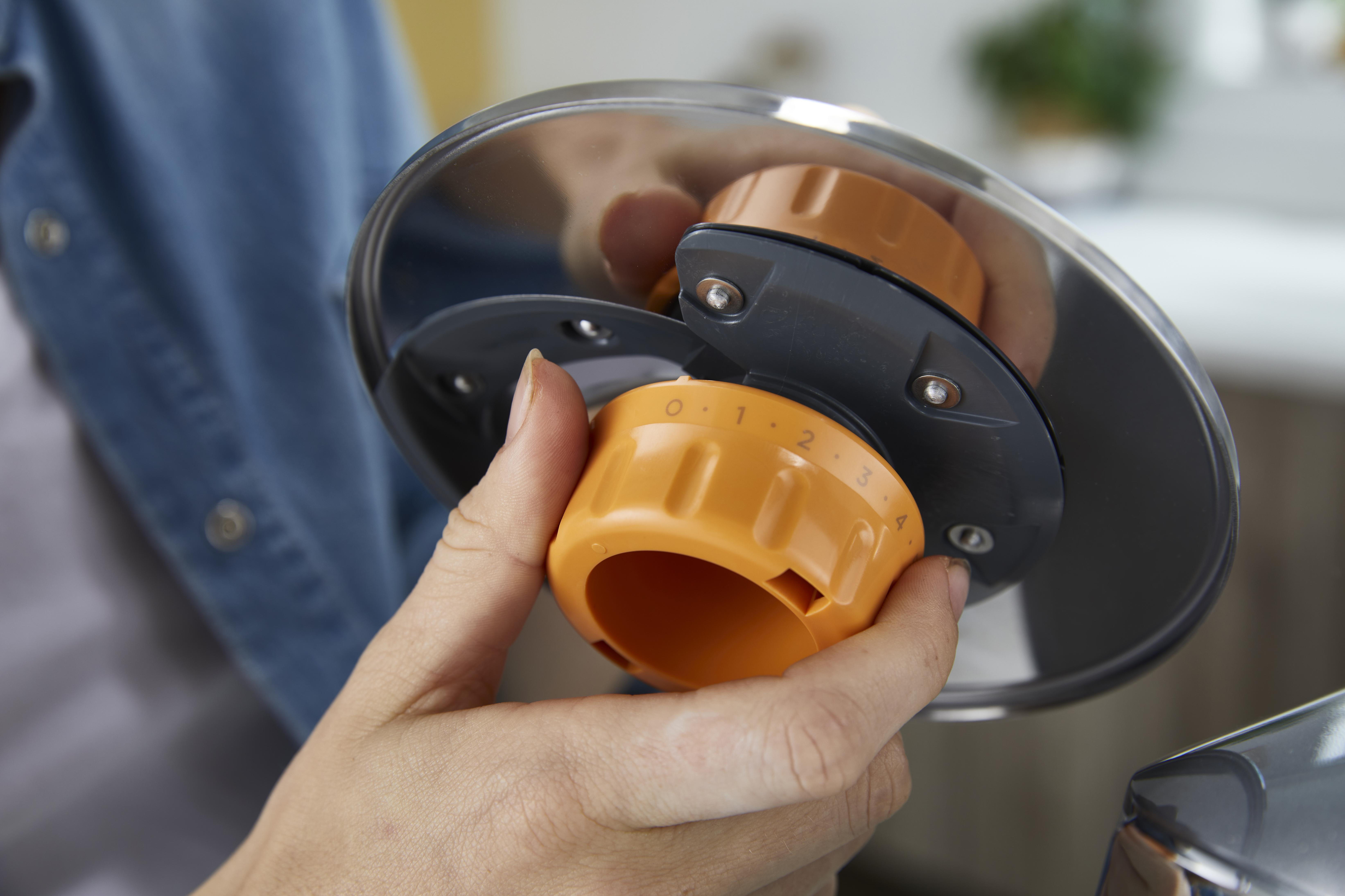 Hände einer Person, die eine silberne Scheibe mit einem grauen Ring und einem orangefarbenen Zifferblatt halten.