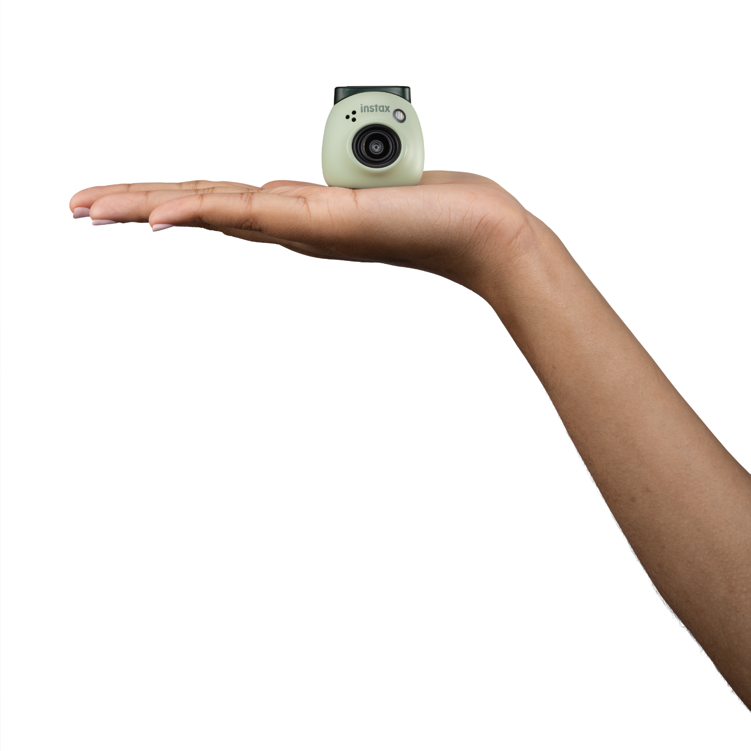 Hand holding a small, light-green Instax camera. Black background. The camera is in focus.
