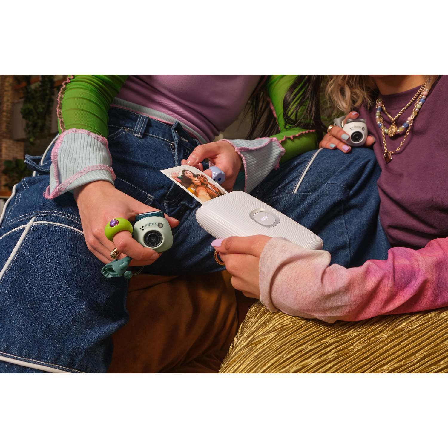 Two people are holding cameras, looking at a printed photo, and sitting in a room.