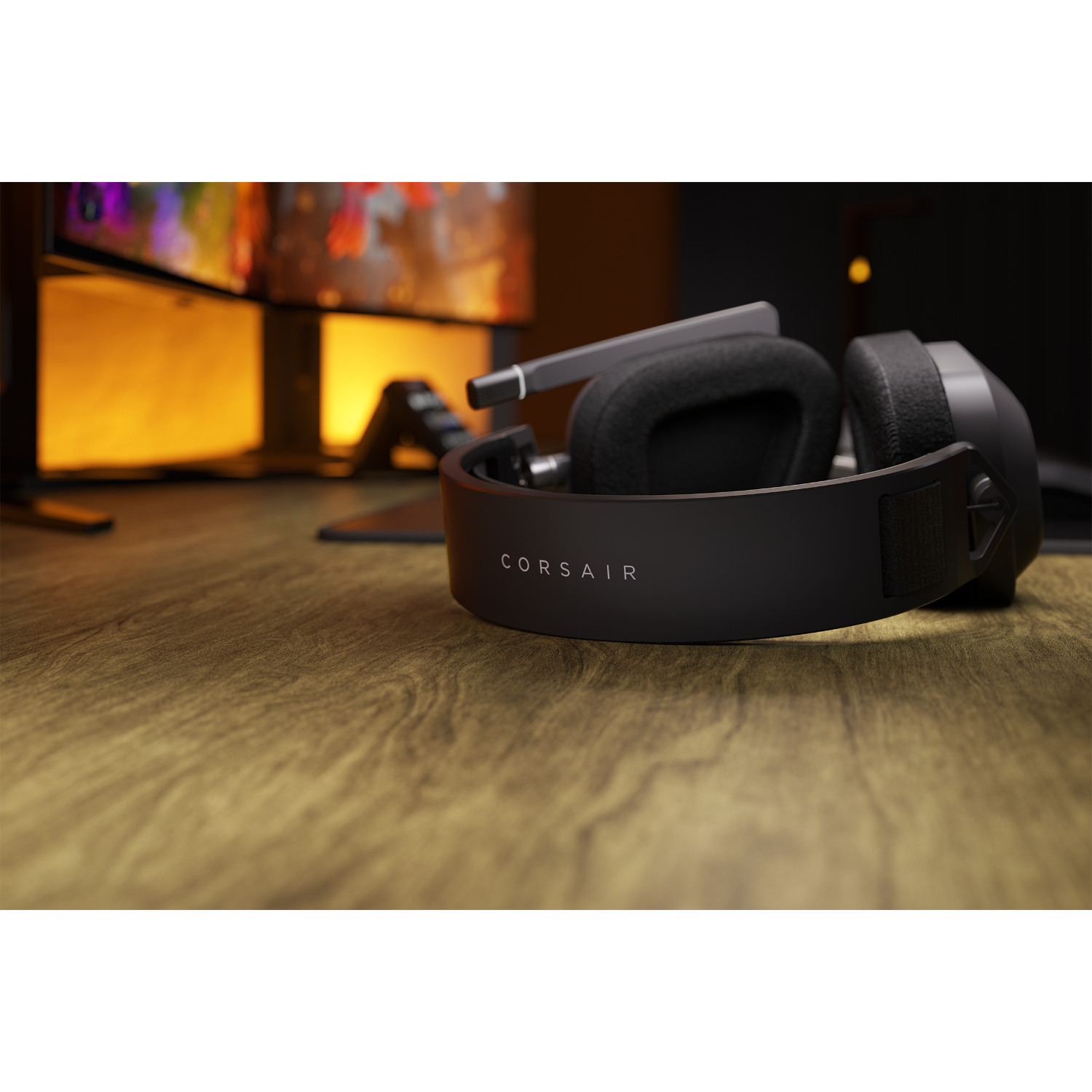 A black Corsair headset on a wooden table, with a monitor in the background. The word 'Corsair' is visible.