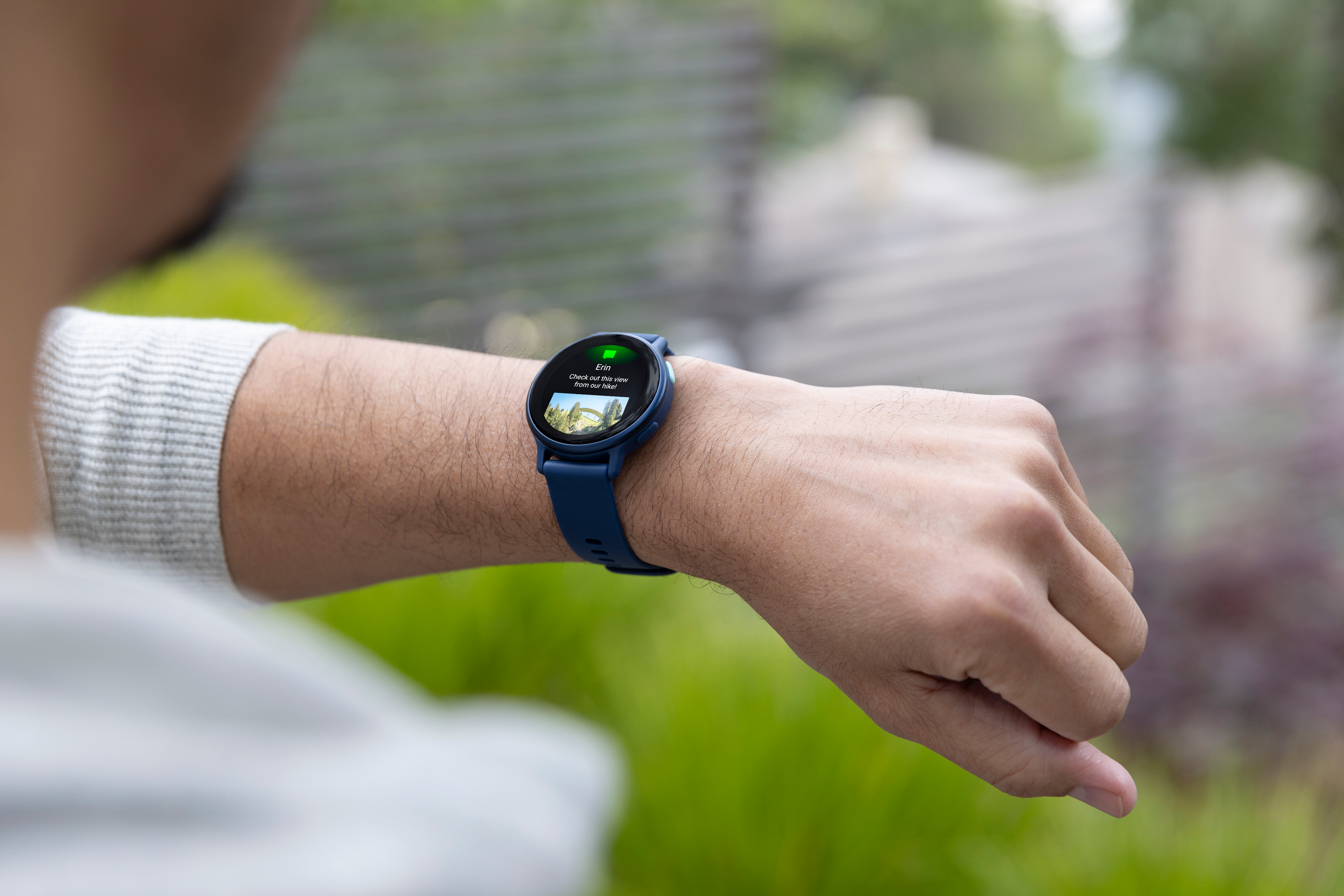 Person mit blauer Smartwatch, die den Bildschirm im Freien mit grünem Hintergrund überprüft.