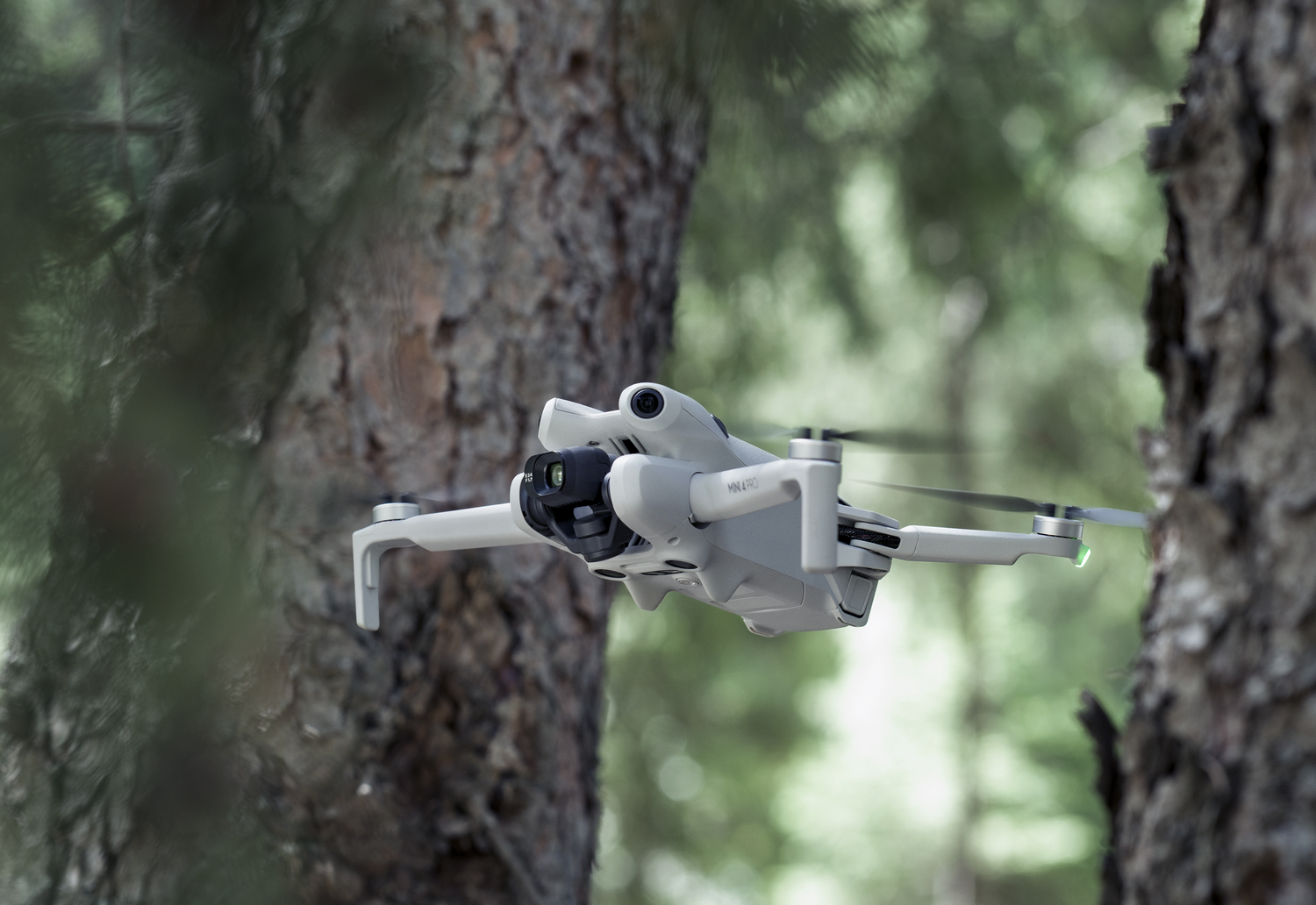 Un dron en vuelo, posicionado entre dos troncos de árboles, con un fondo de bosque.