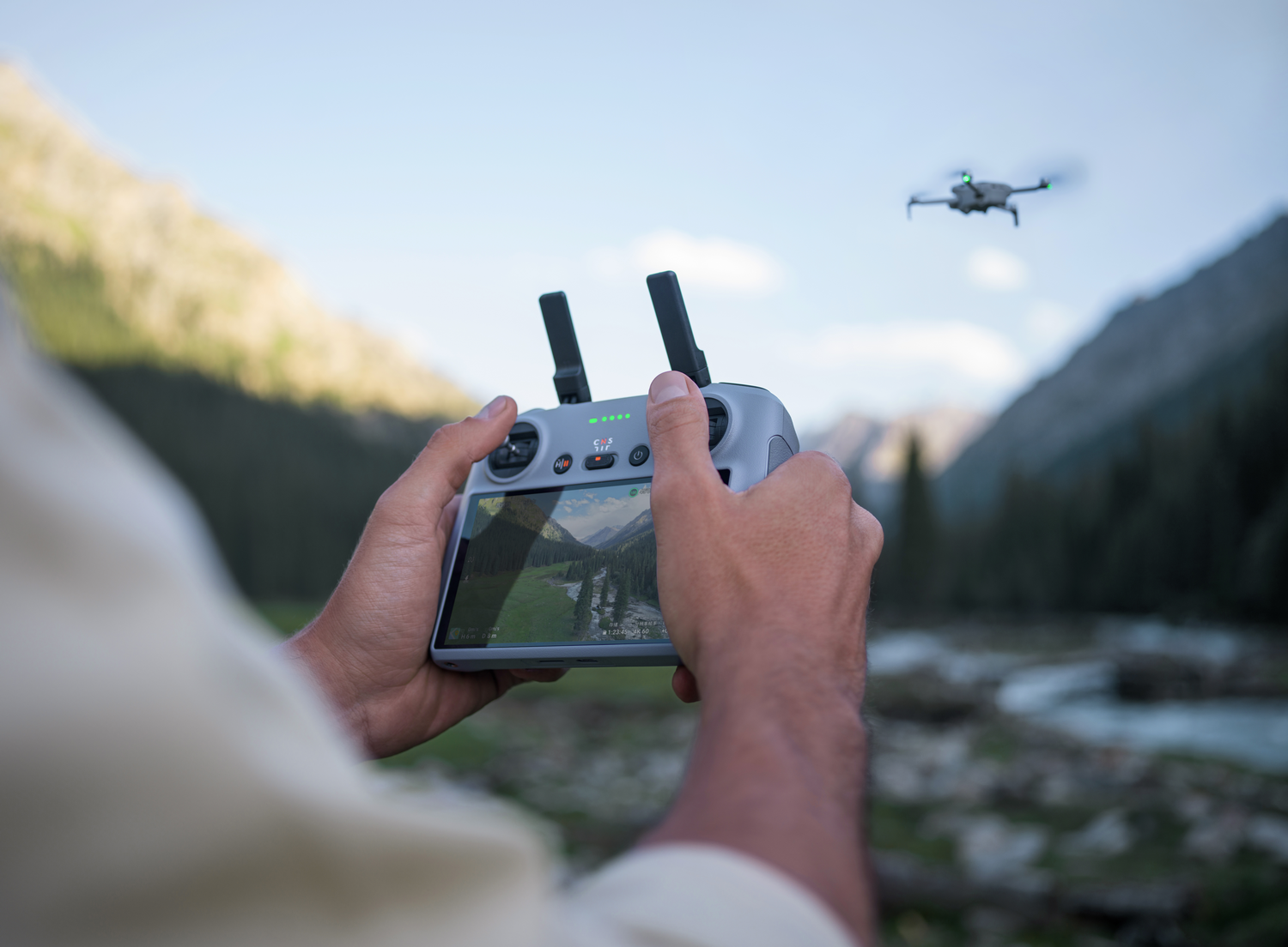 Persona sosteniendo control de dron, dron en el cielo con montañas de fondo.