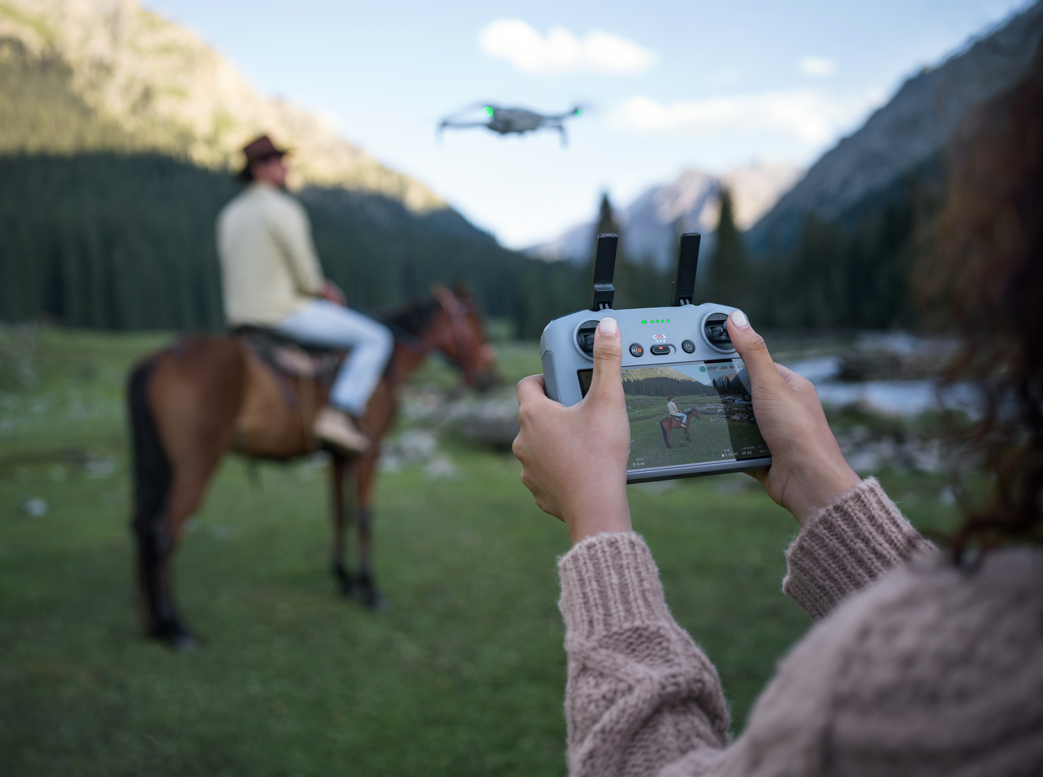 Persona usando un controlador de dron, persona montando a caballo en el fondo.