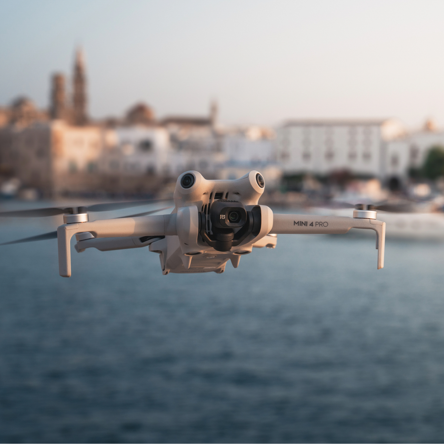 Drone in volo sull'acqua, edifici sfocati sullo sfondo.