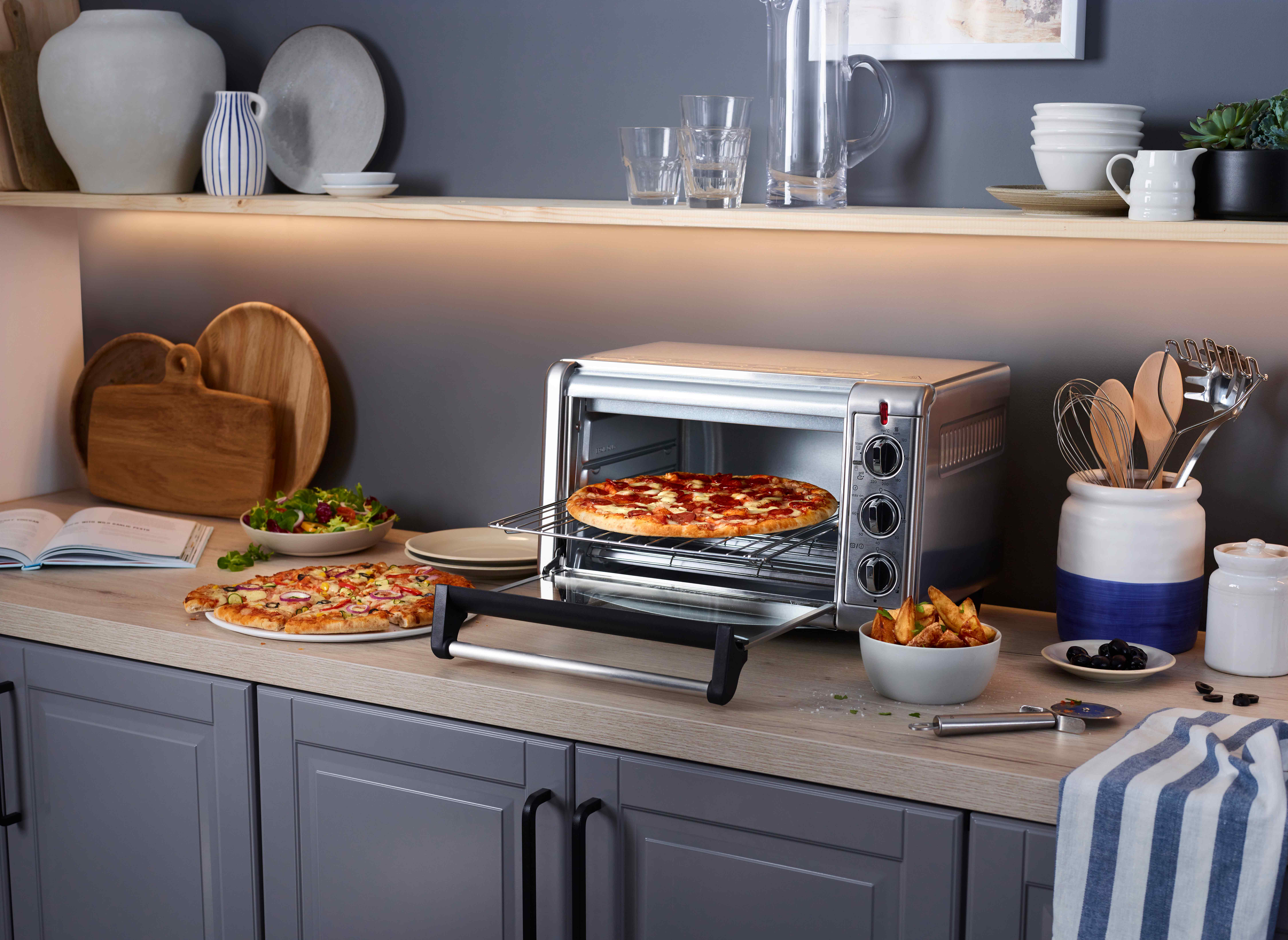 Egy kenyérpirító sütő pizza és sült krumplival. Étel a pulton konyhai háttérrel.