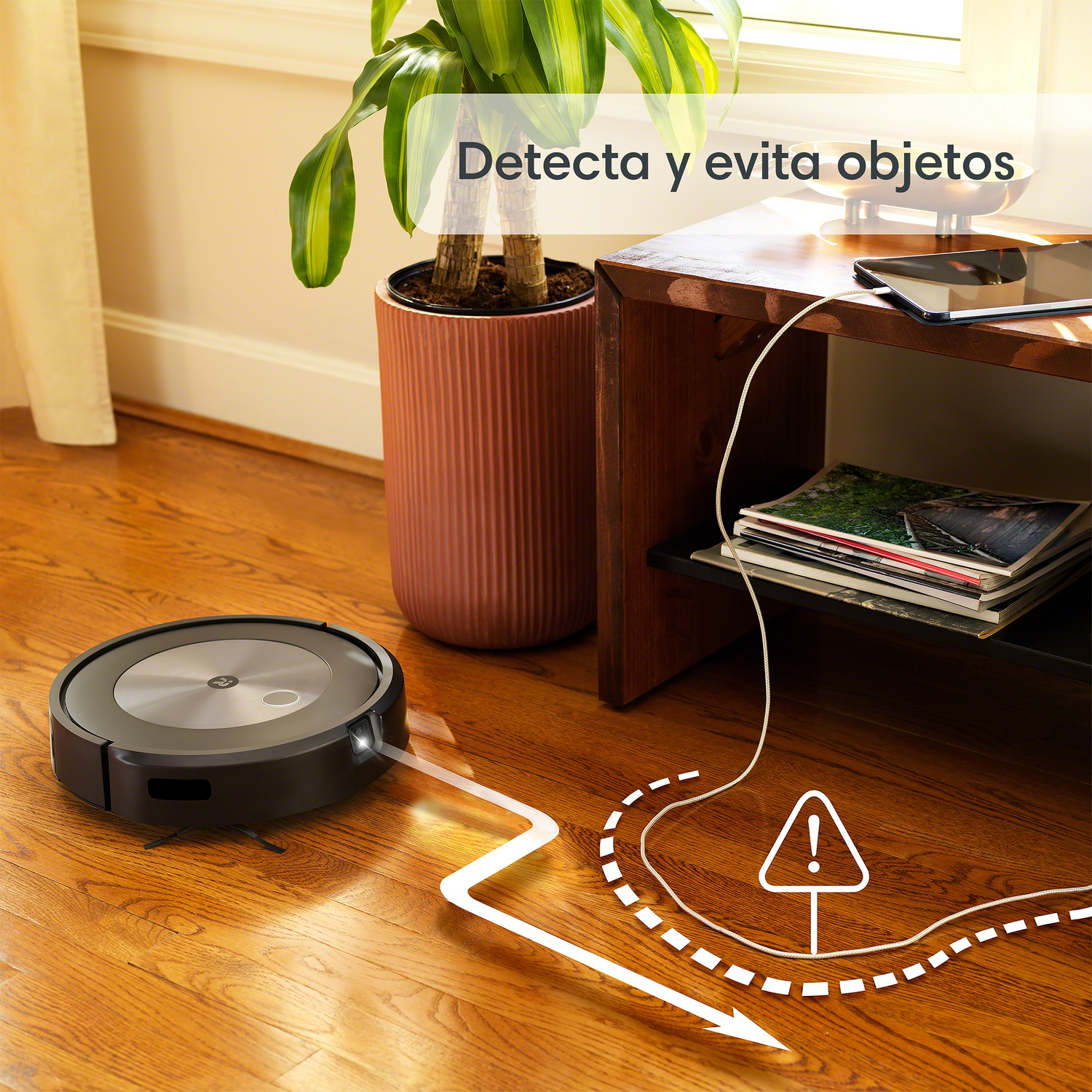 Robot aspirador en suelo de madera, con una planta al fondo.