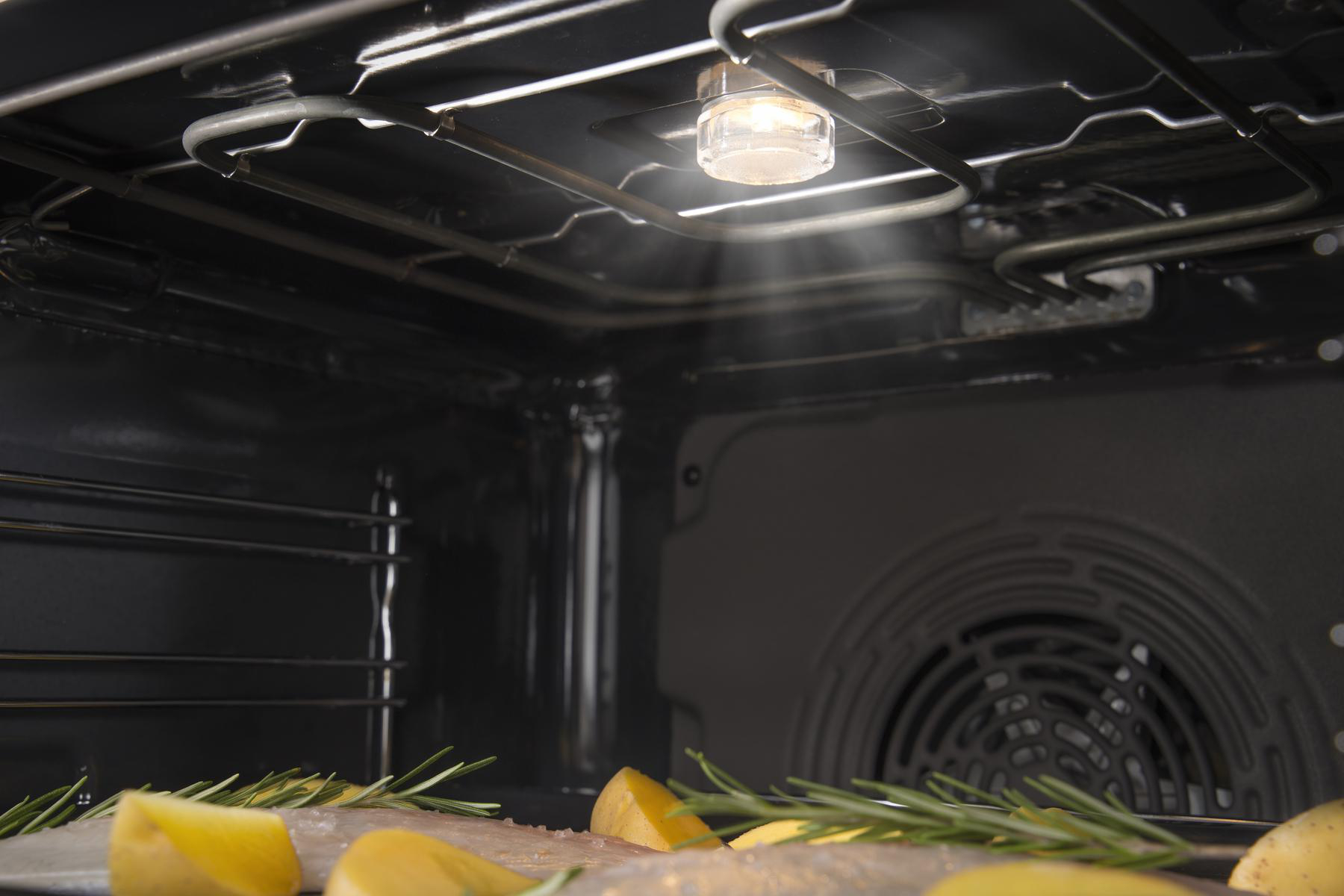 Ein Backofeninnenraum mit Essen, beleuchtet von einem Licht von oben. Kartoffelscheiben sind sichtbar.