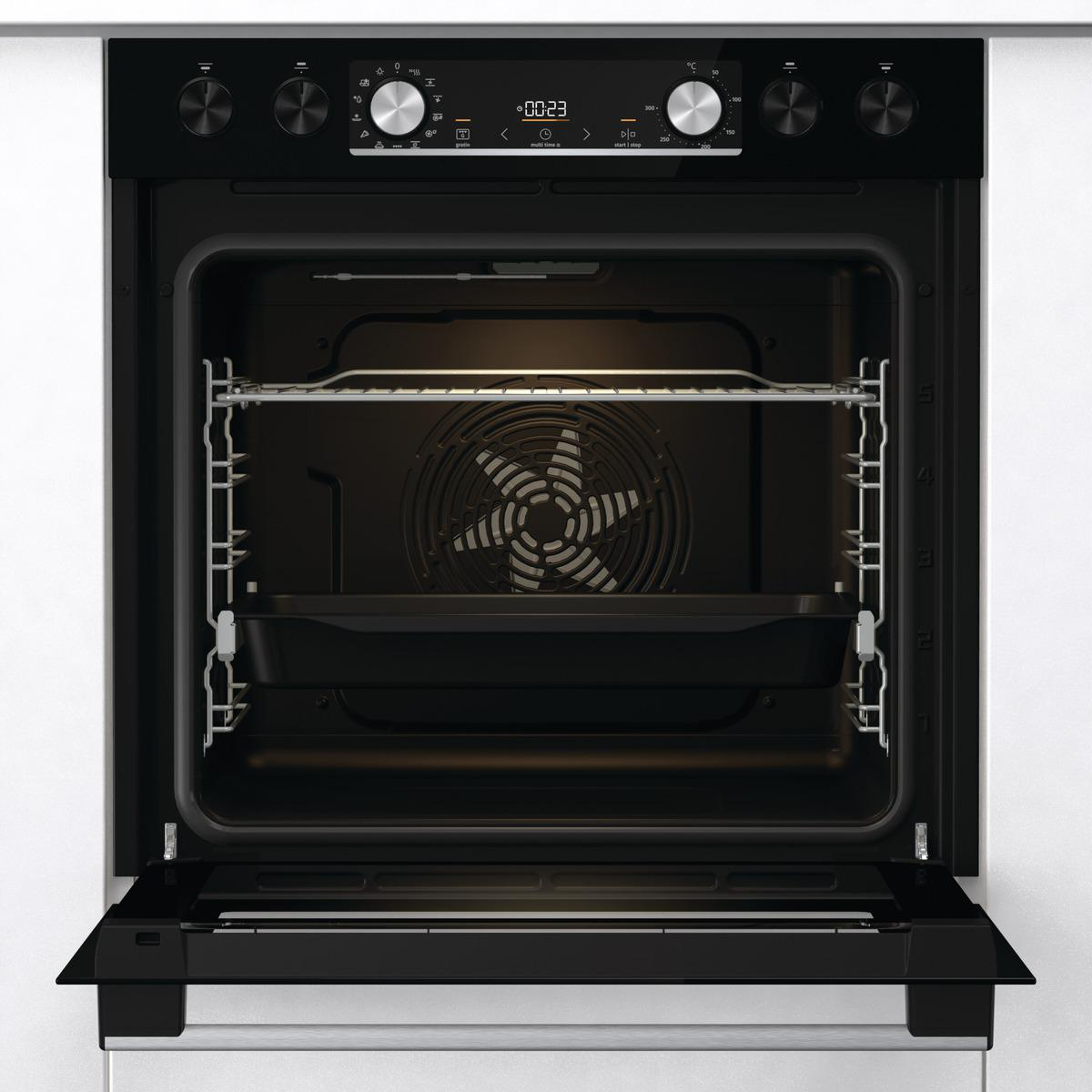 Ein Backofen-Innenraum, offen, mit schwarzem Blech und Lüfter, in einem weißen Schrank.