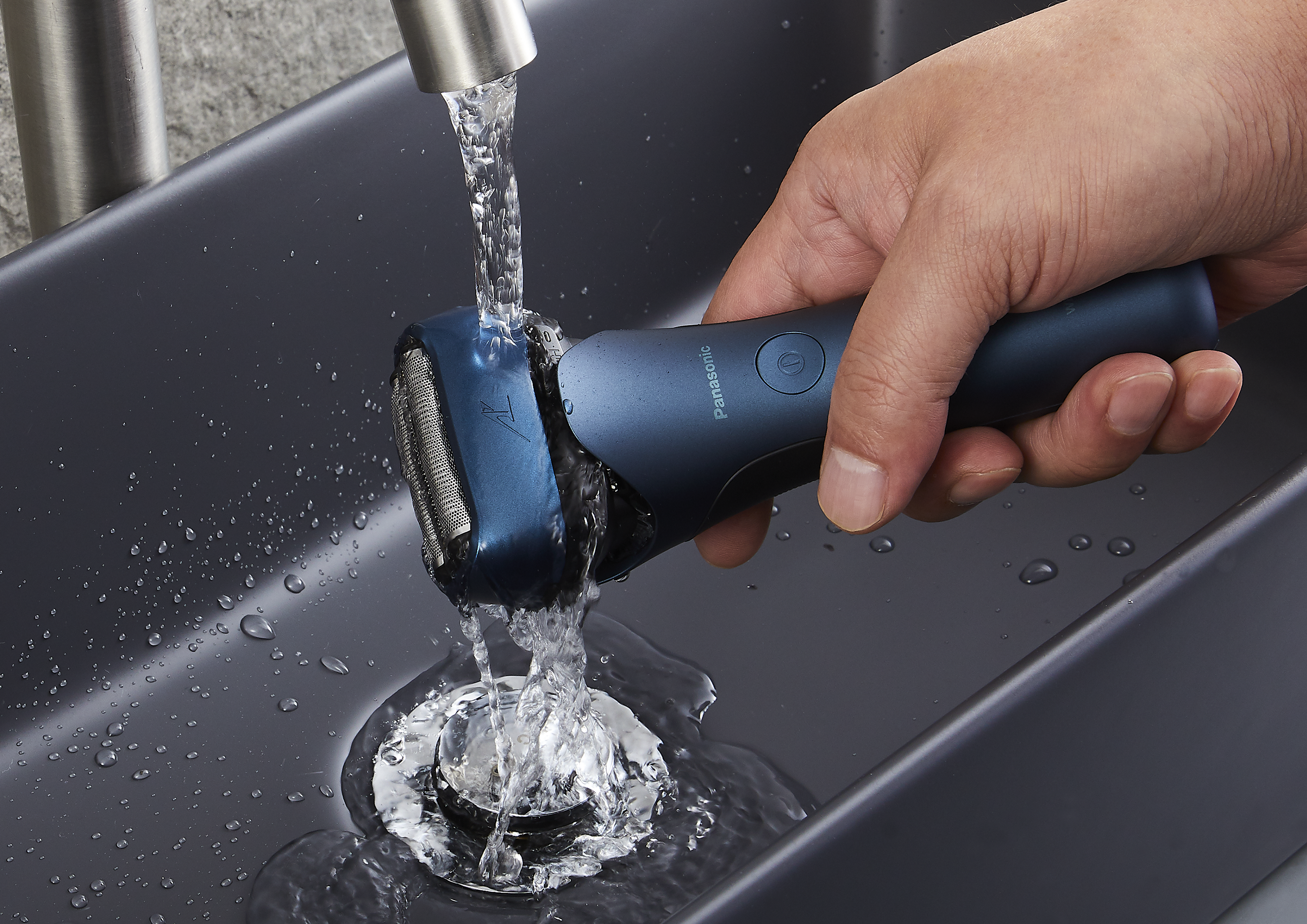 Eine Hand spült einen blauen Elektrorasierer unter fließendem Wasser.