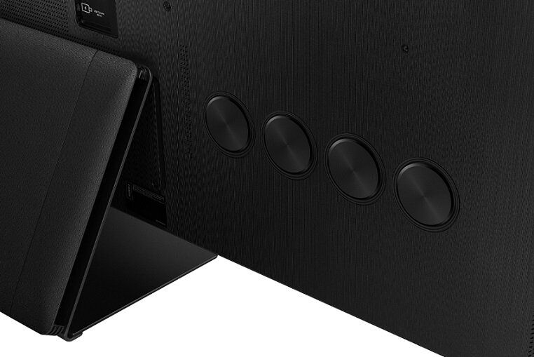 Zbliżenie tylnego panelu czarnego telewizora, pokazujące cztery okrągłe kratki głośnikowe.