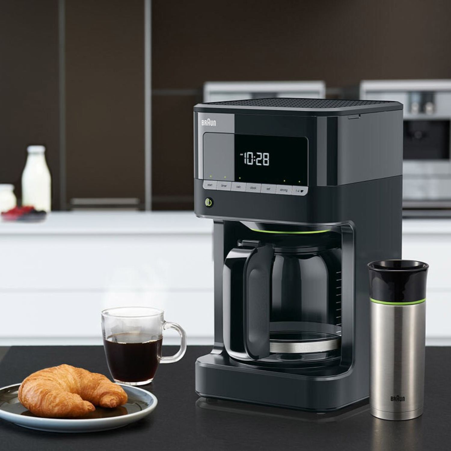 A black coffee maker with a cup of coffee, croissant, and a thermos.