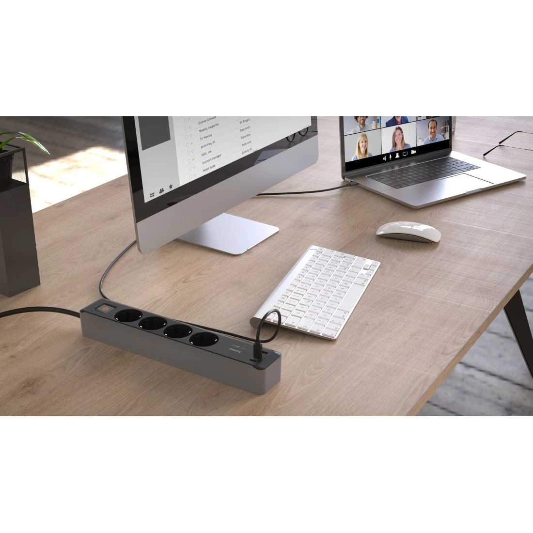 Escritorio de oficina con monitor de ordenador, portátil, teclado, ratón y regleta con enchufes.