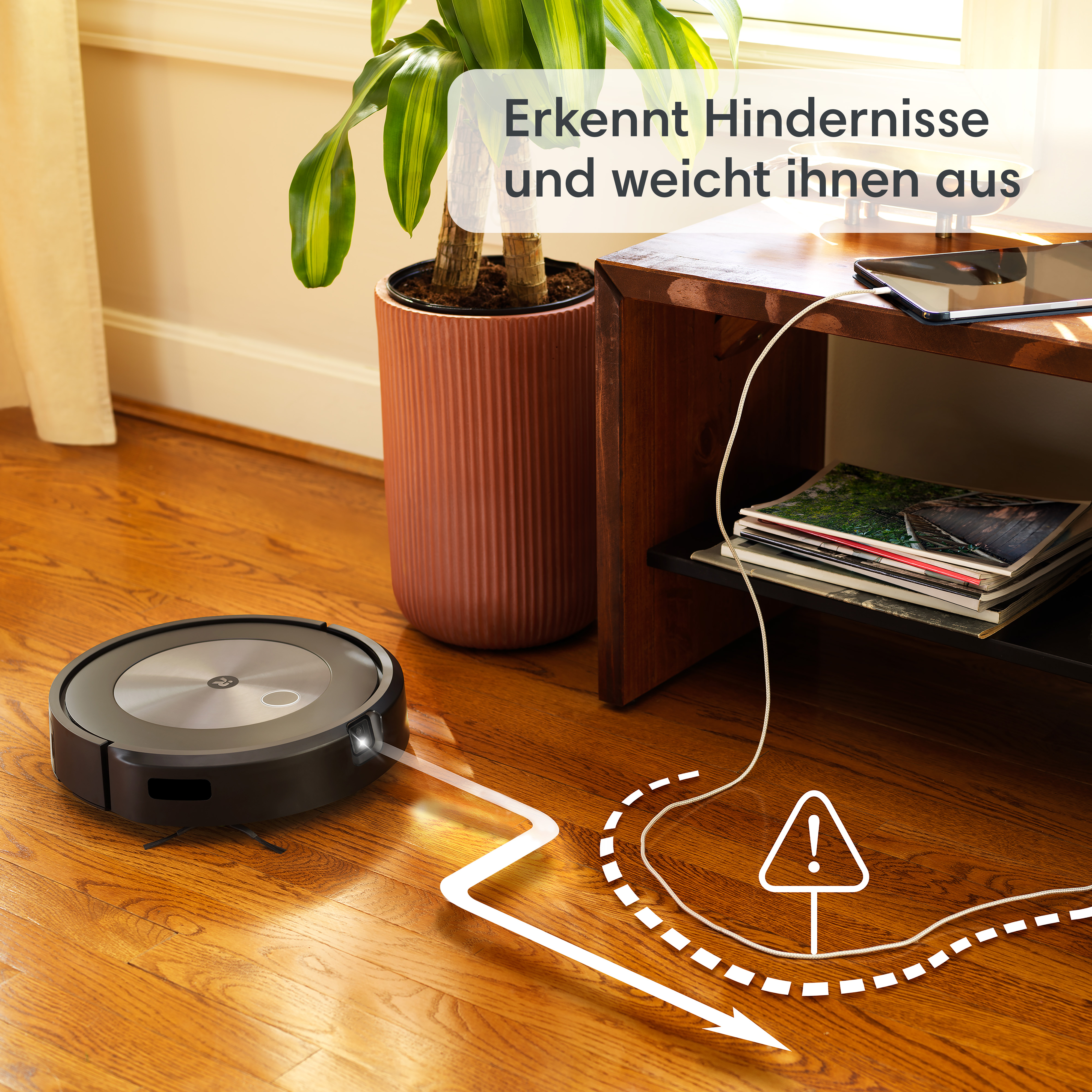 Ein schwarzer Roboter-Staubsauger reinigt einen Holzboden, mit Pflanze und Möbeln im Hintergrund.