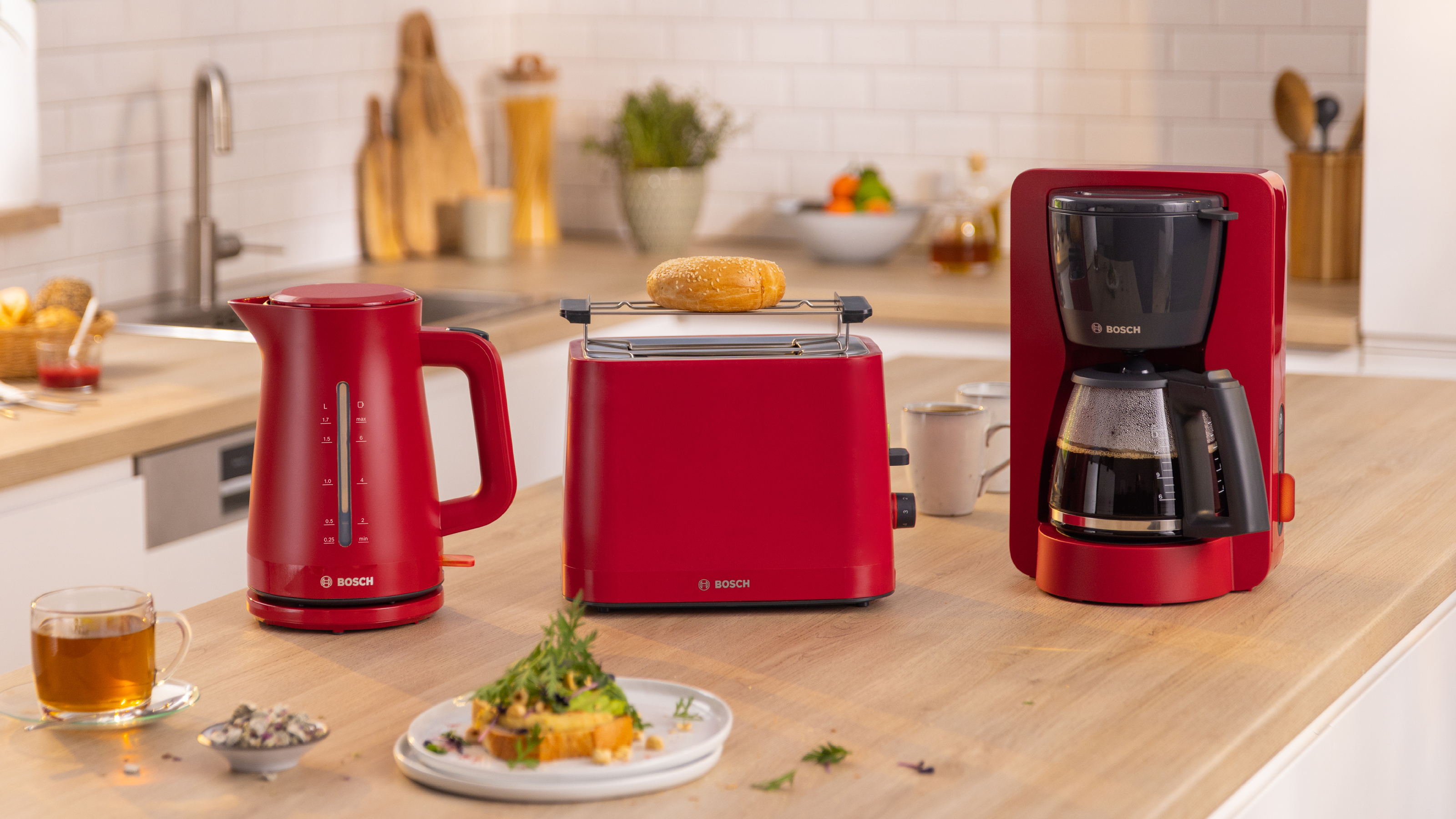 Rote Küchengeräte: Wasserkocher, Toaster mit Bagel und Kaffeemaschine auf der Theke.