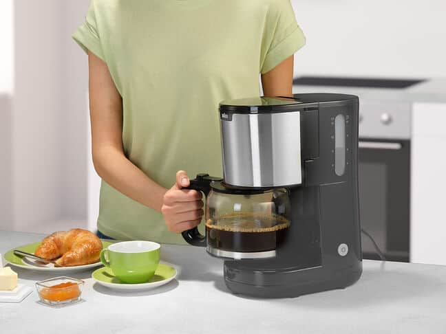 Frau gießt Kaffee aus einer schwarzen Kaffeemaschine in eine Glaskaraffe.