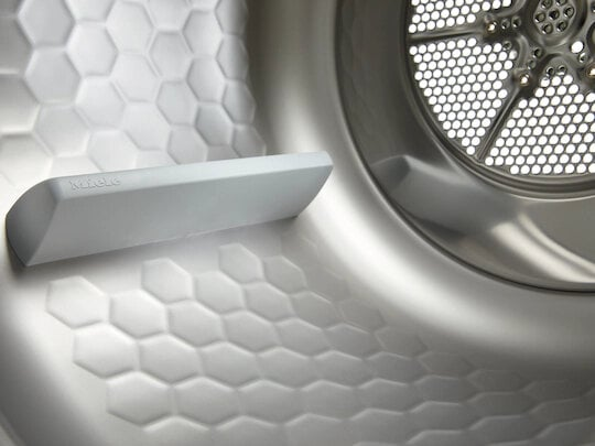 Wnętrze suszarki. Biały wzór plastra miodu, szara łopatka i metalowy bęben.