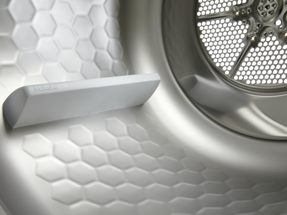 Zbliżenie wnętrza suszarki, pokazujące biały filtr na kłaczki i metal o strukturze plastra miodu.