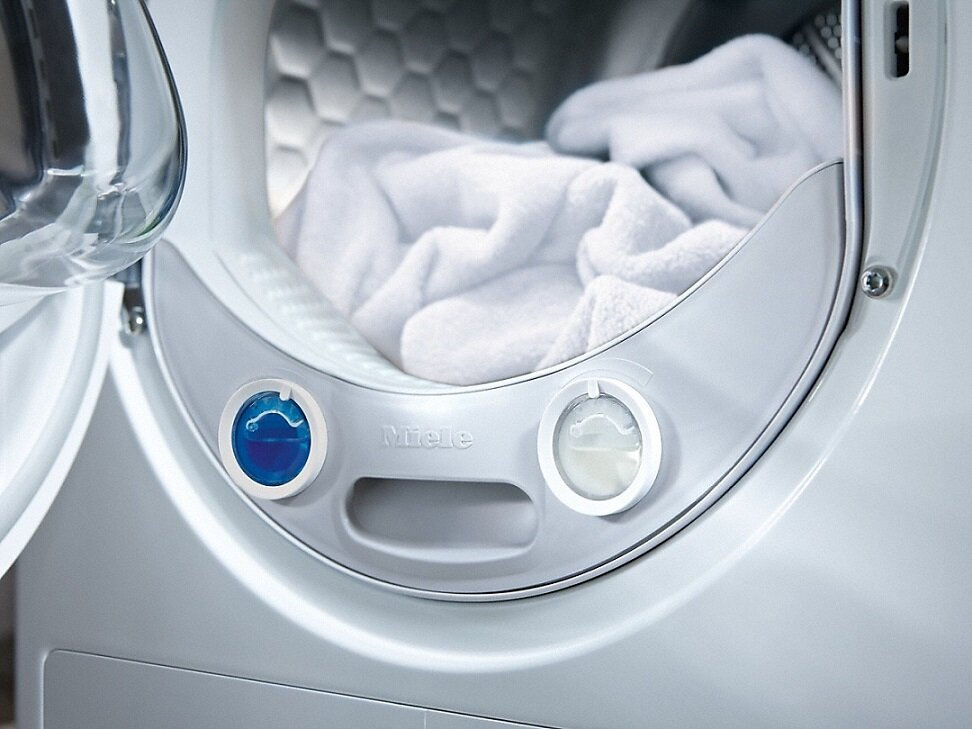 Wnętrze pralki z białymi ręcznikami. Na froncie widoczne są niebieskie i białe pokrętła.