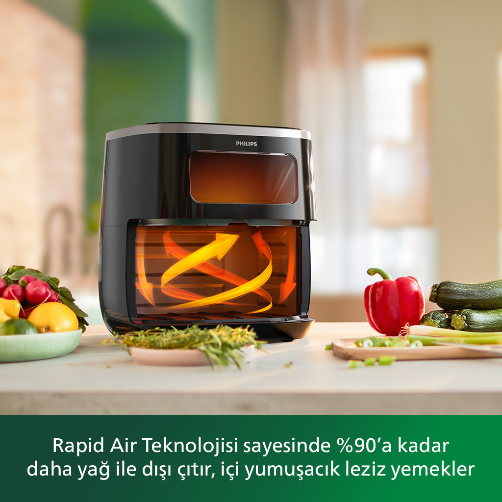 İçinde yiyecek olan siyah ve gümüş Philips fritözü. Önünde masada portakallar var.