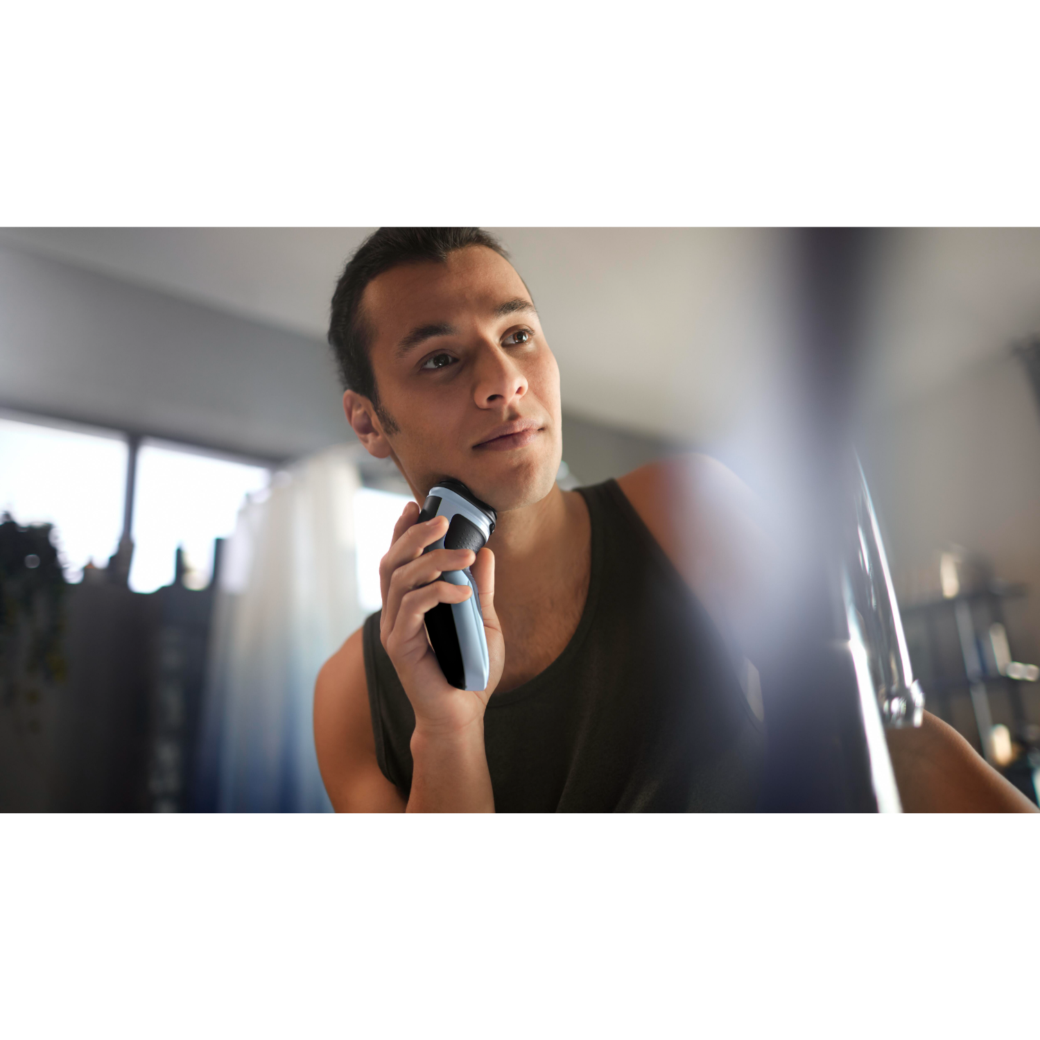 Man shaving his face with an electric shaver in a bathroom.