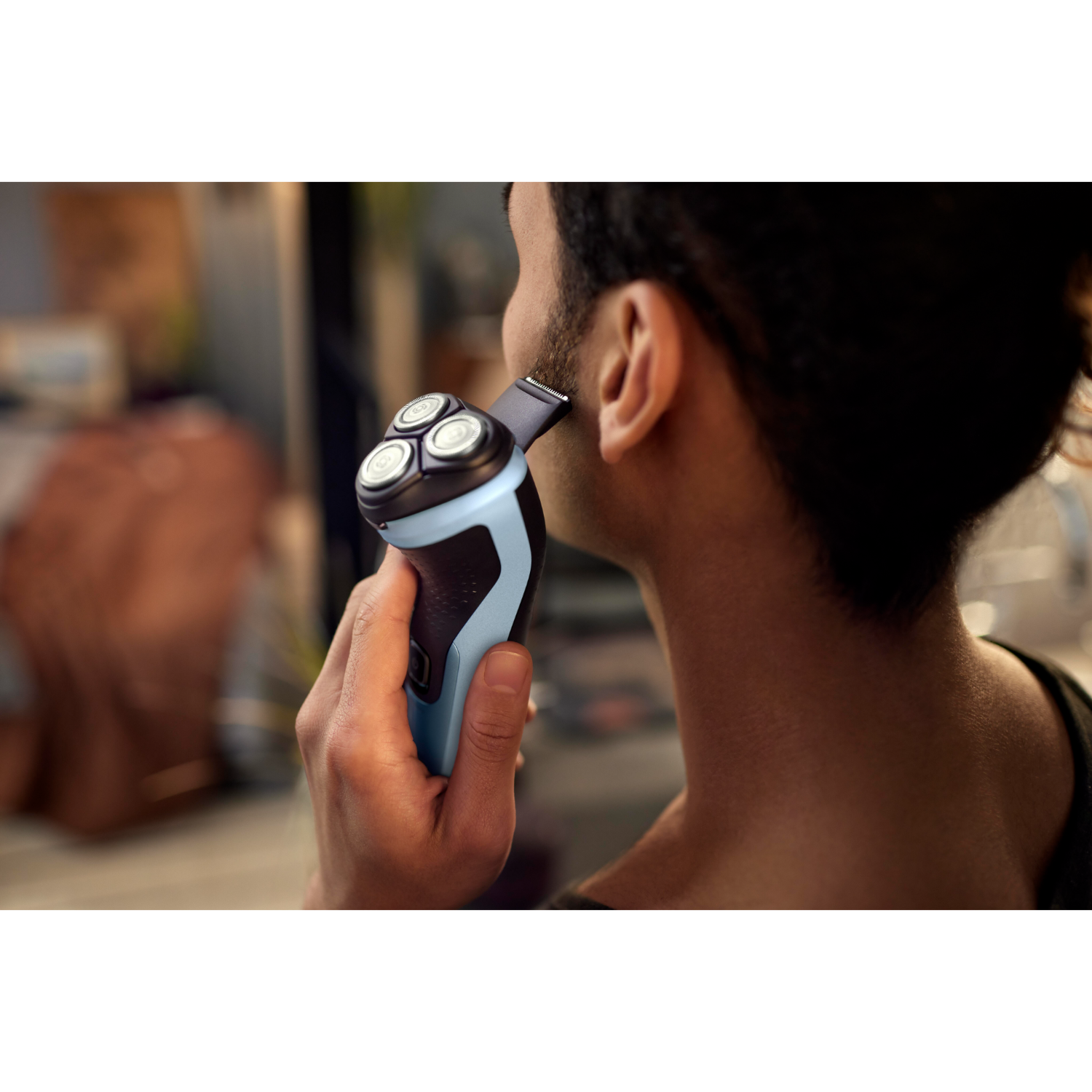A man shaves his face with an electric shaver. The shaver is blue and black. The man has dark hair.