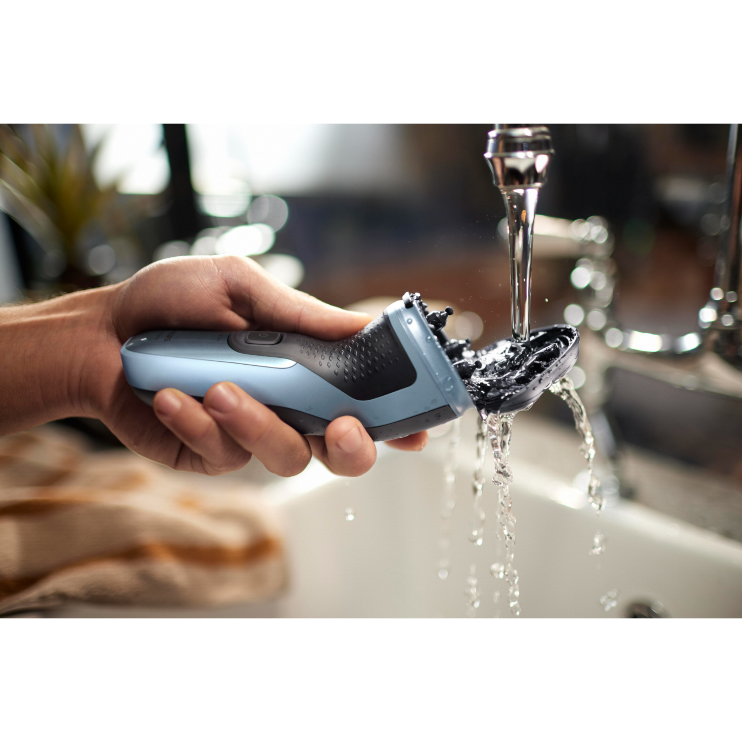 A person's hand holding a blue and black electric shaver under running water.