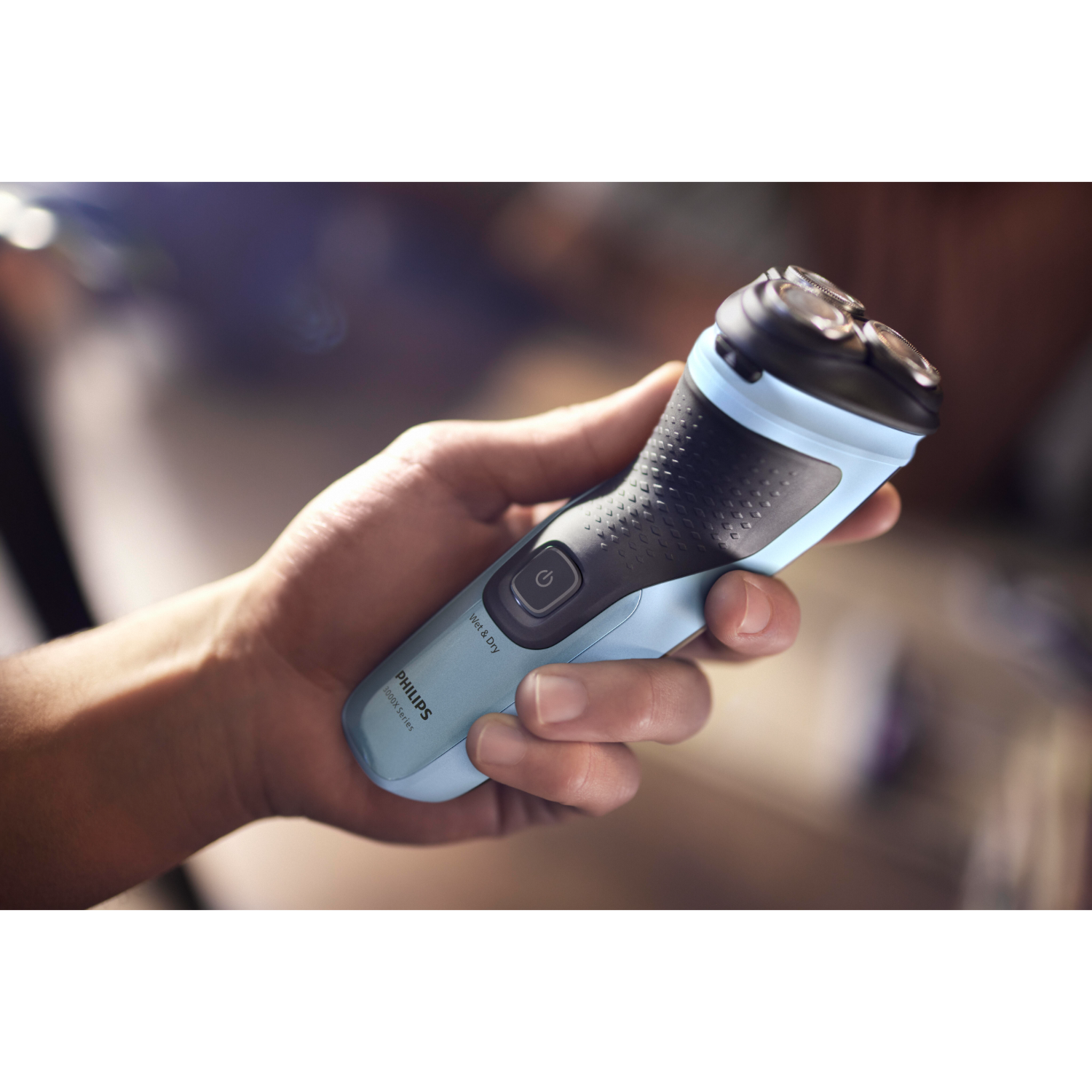 Man holding a blue and black Philips electric shaver. Blurred background.