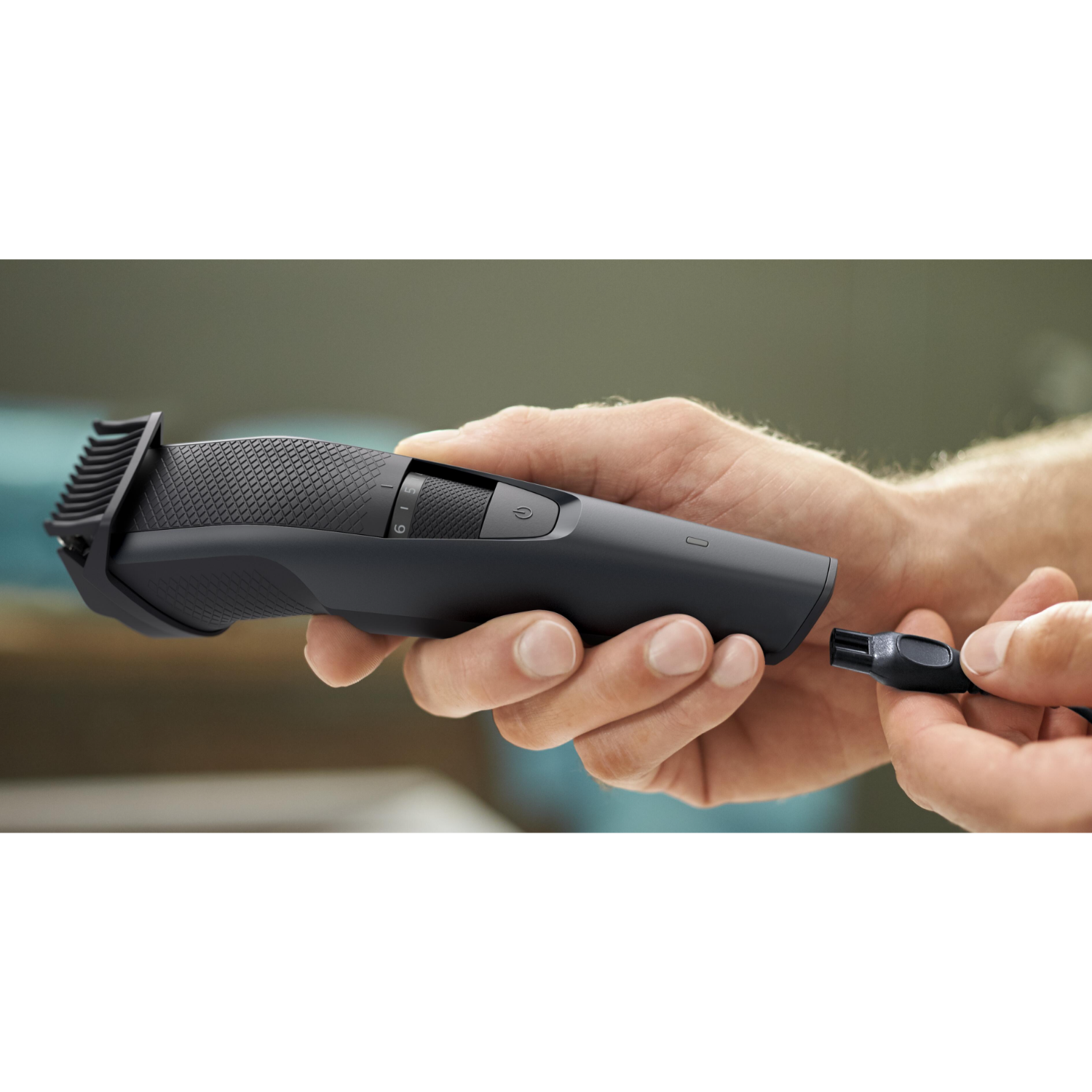 A black Philips beard trimmer being held, with a small brush.