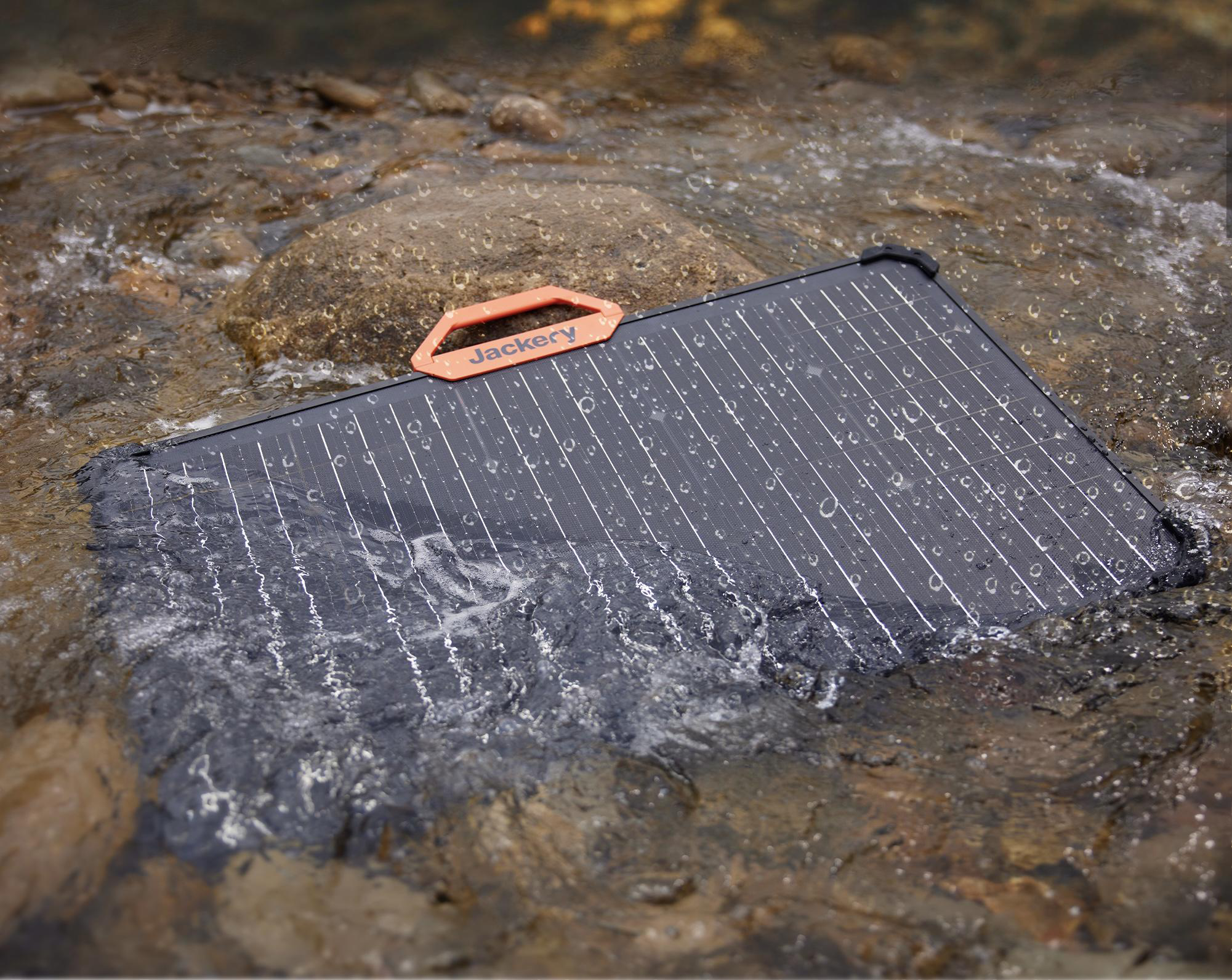 Schwarzes Solarpanel in fließendem Wasser mit orangefarbenem Griff und Jackery-Logo.