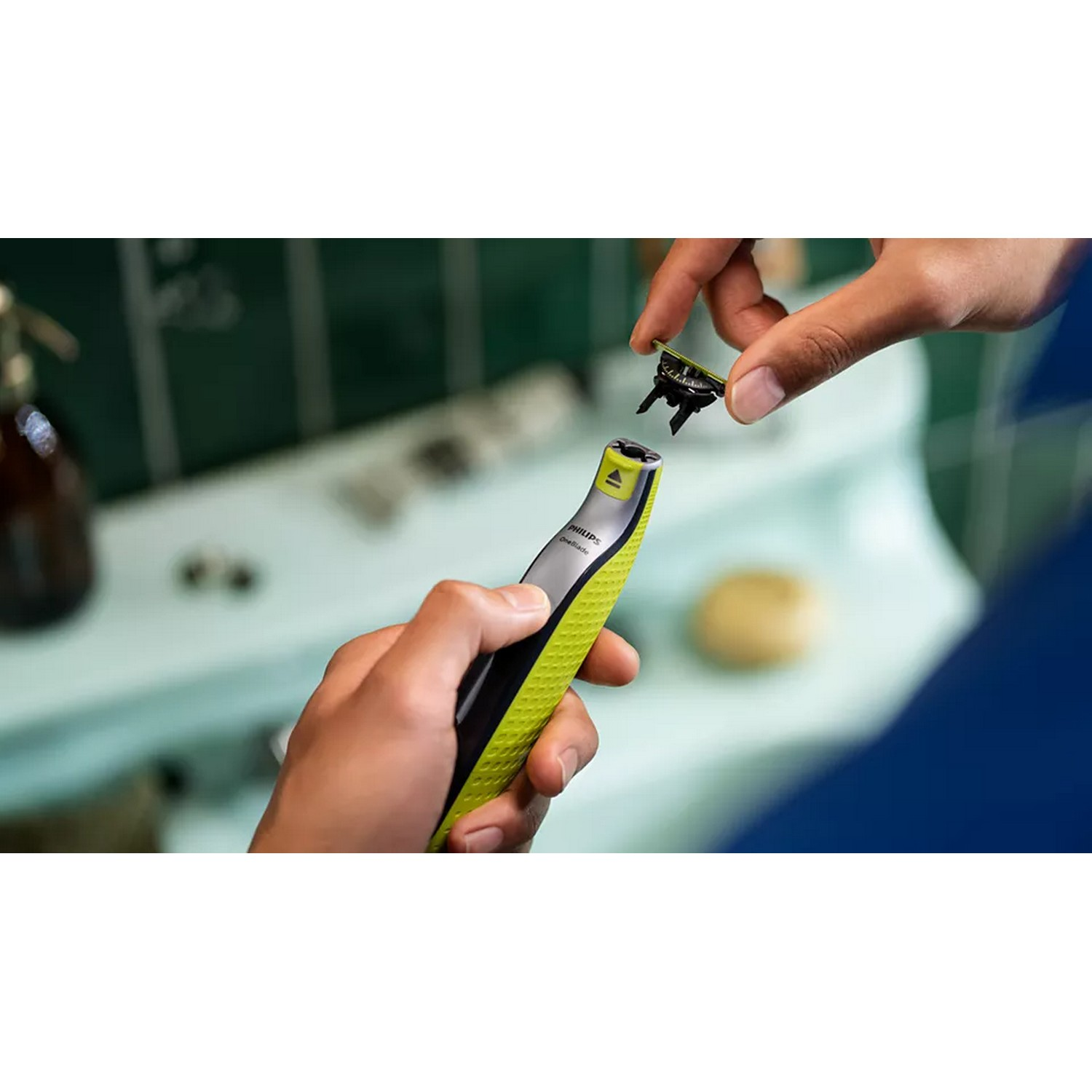 A person holding a Philips OneBlade razor, with a blade detached, in a bathroom setting.