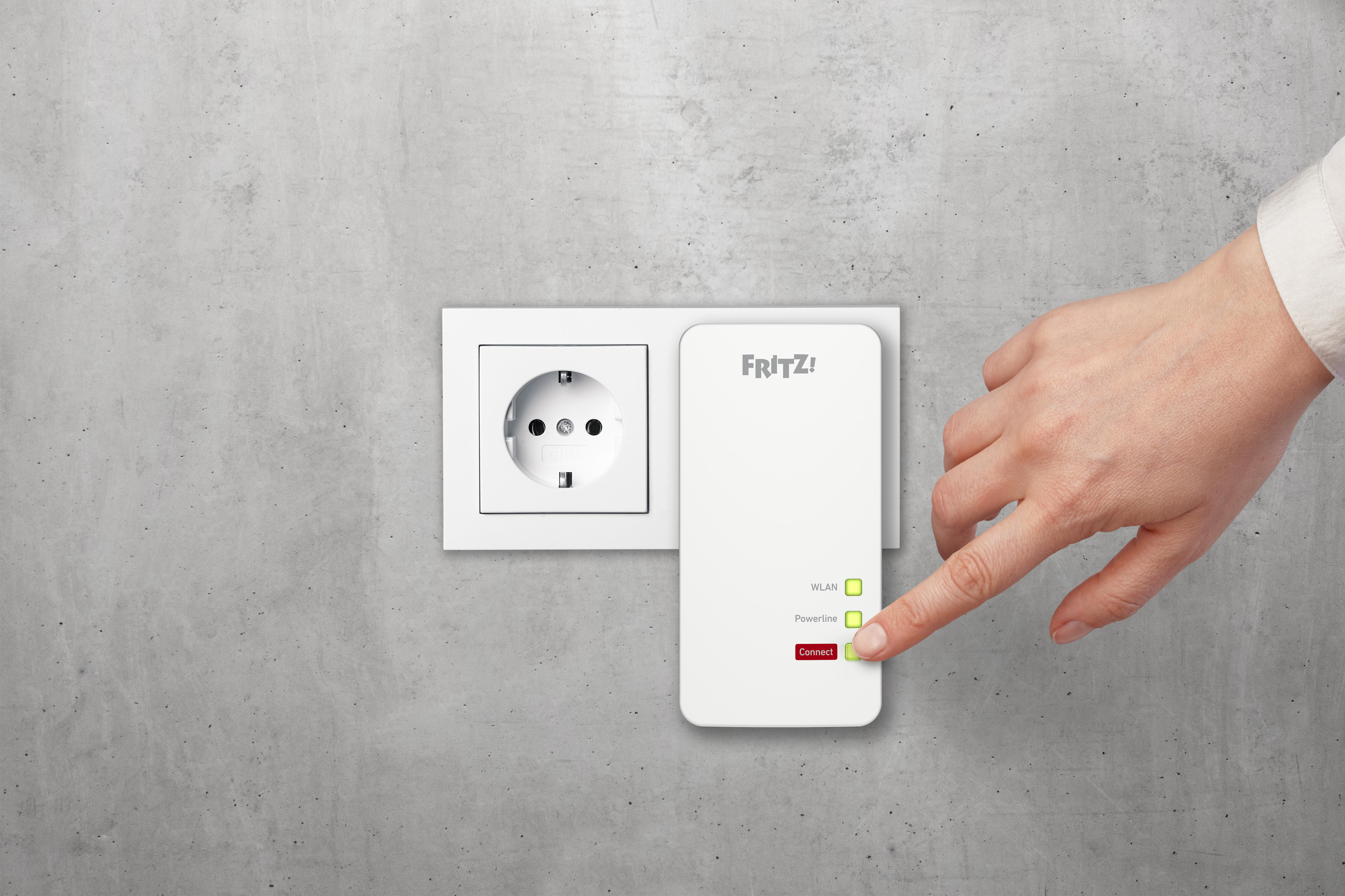 Weißer Powerline-Adapter in einer Steckdose, ein Finger zeigt auf eine Taste.