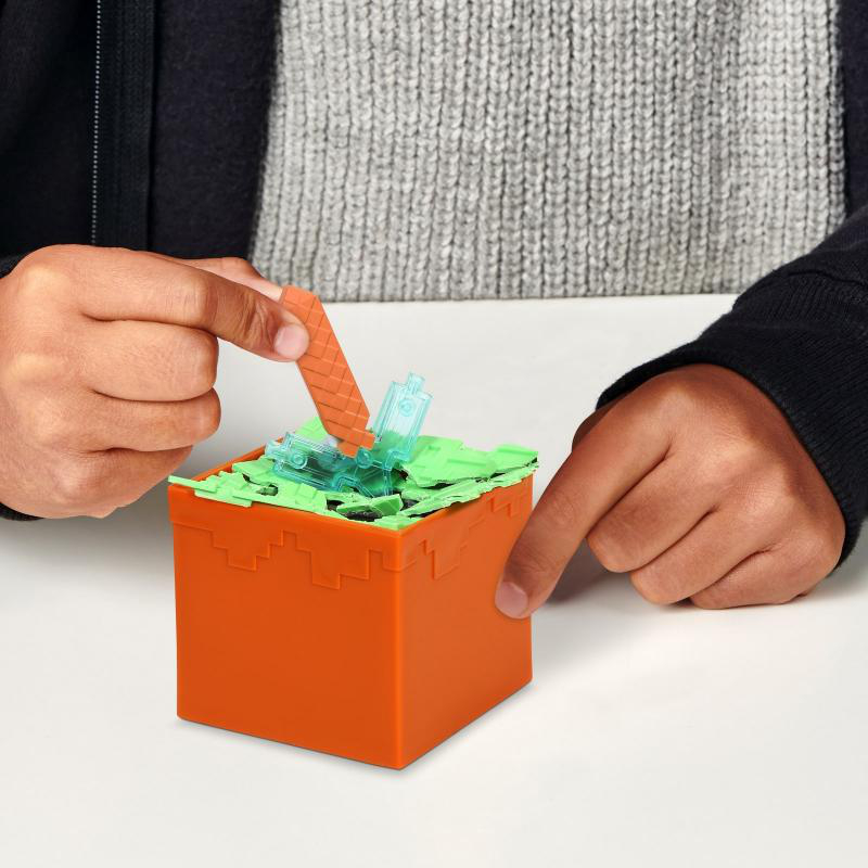 Hände einer Person spielen mit einem Minecraft-Spielzeug, platzieren Blöcke in einer Box.