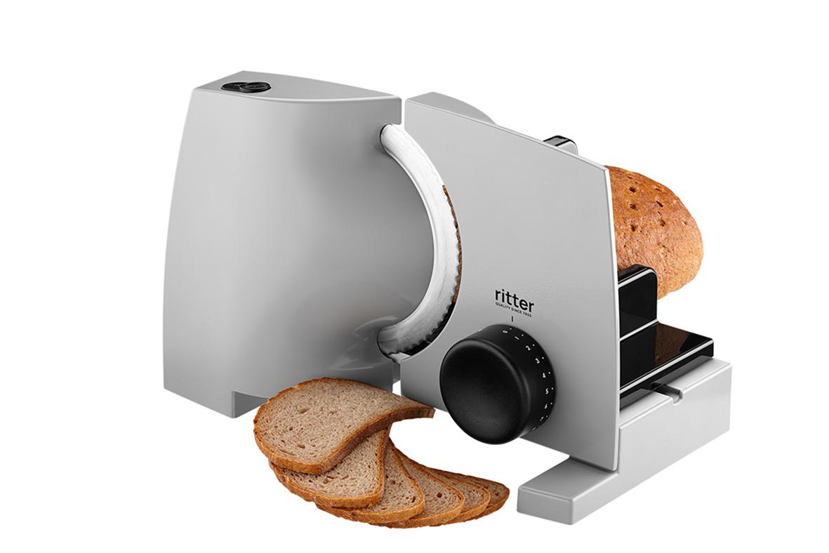 Silberner Brotschneider mit Brotlaib und Scheiben. Maschine auf weißer Oberfläche. Marke Ritter.