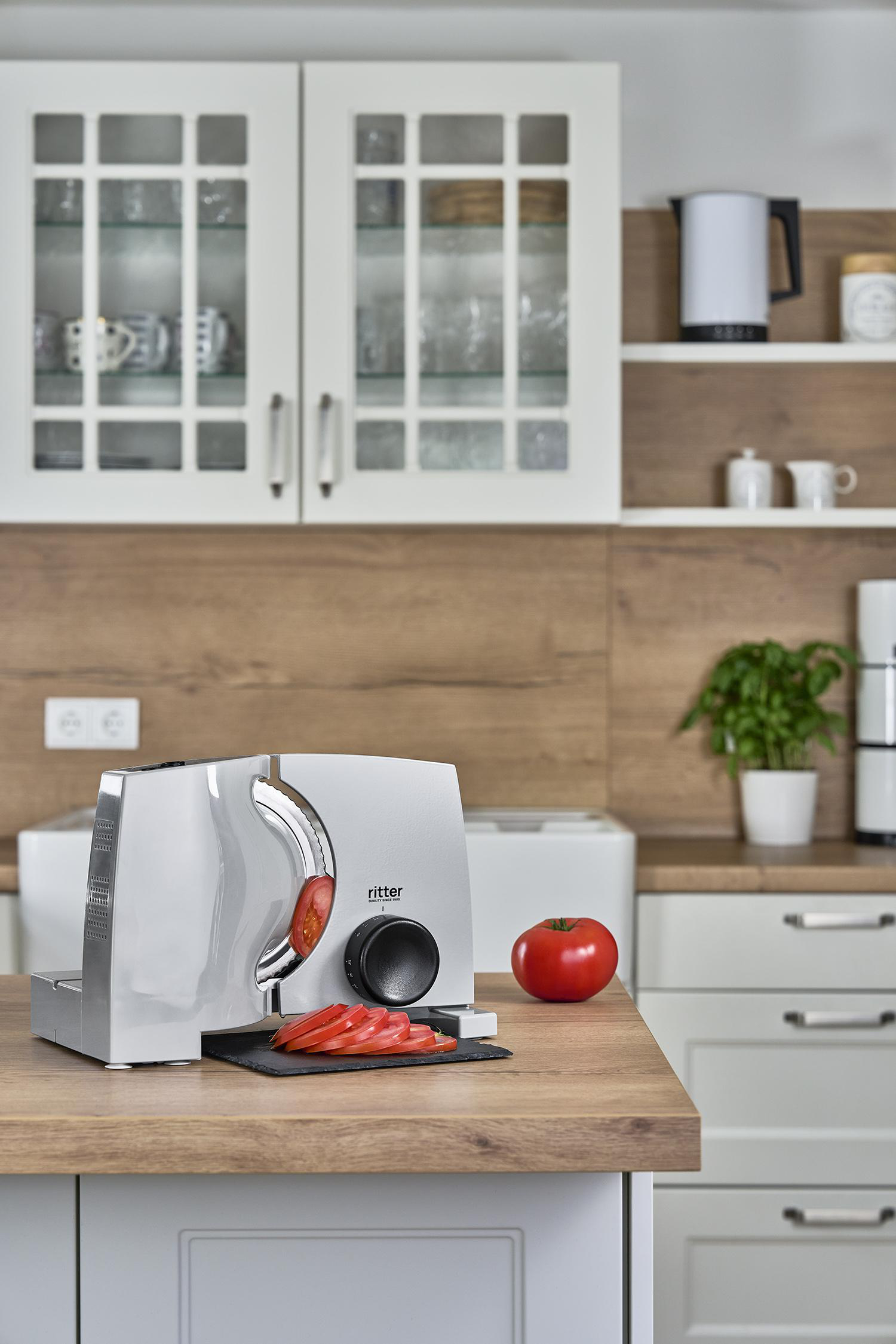 Eine Küchenszene mit einem Schneider, geschnittenen Tomaten und einem Apfel auf einer Holztheke.