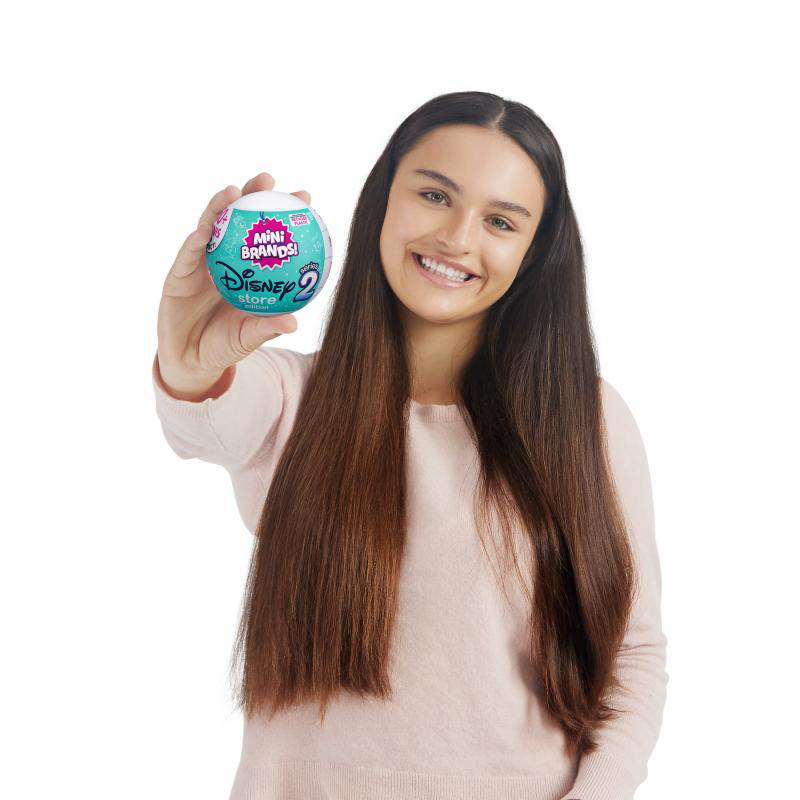 Frau hält einen Disney Mini Brands Ball, lächelt in die Kamera.