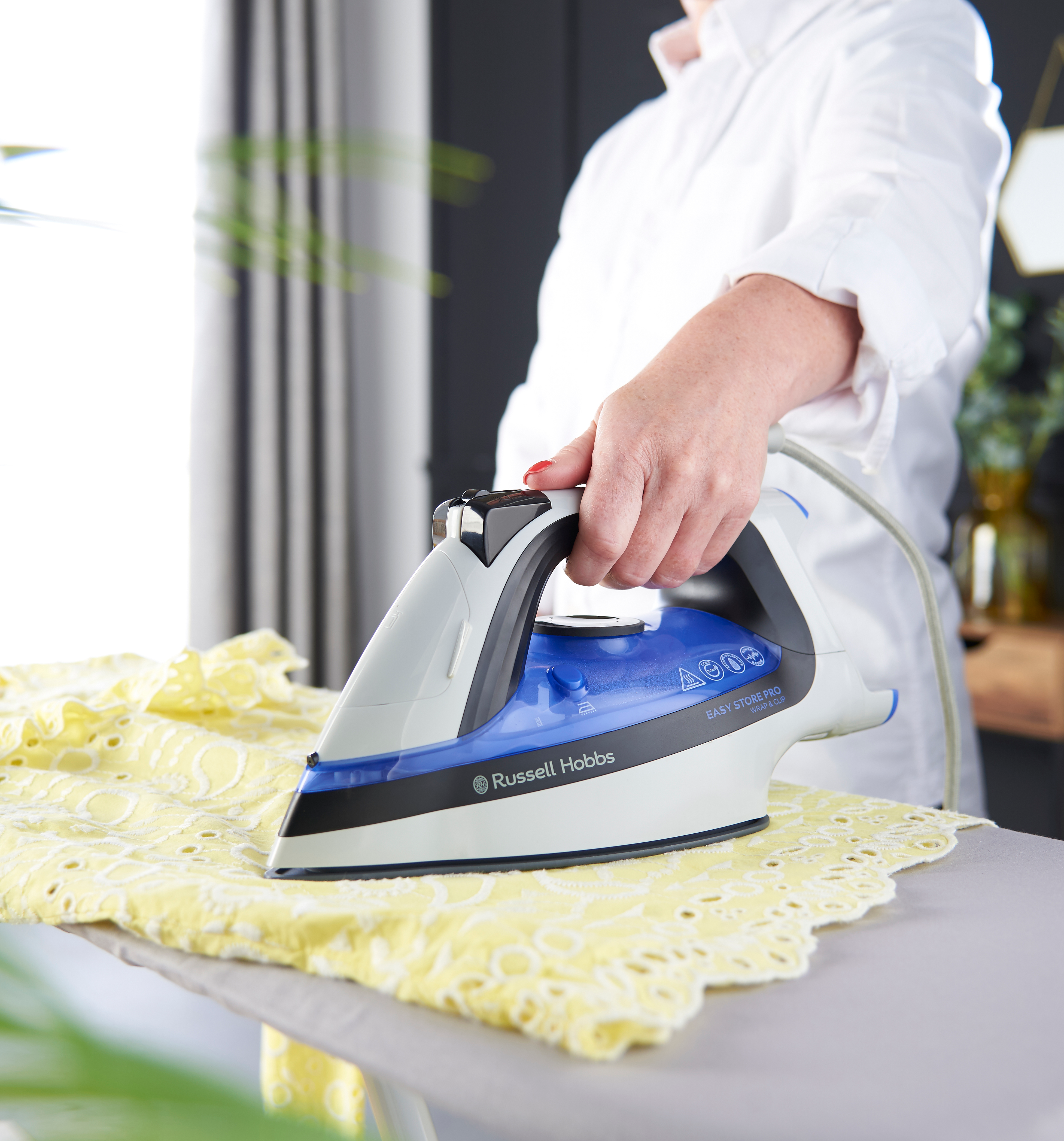 Egy személy sárga anyagot vasal Russell Hobbs vasalóval egy vasalódeszkán.