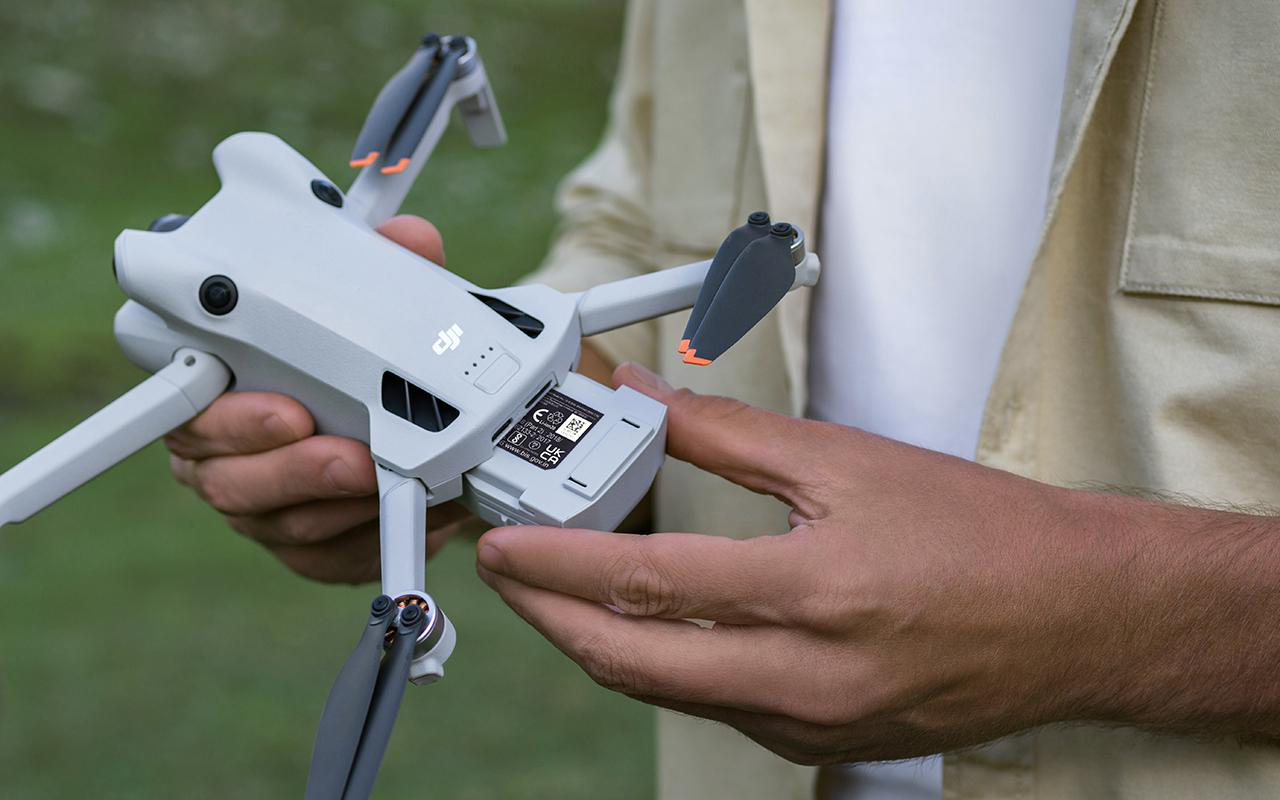Hände einer Person halten eine DJI-Drohne, bereiten das Einsetzen eines Akkus vor.